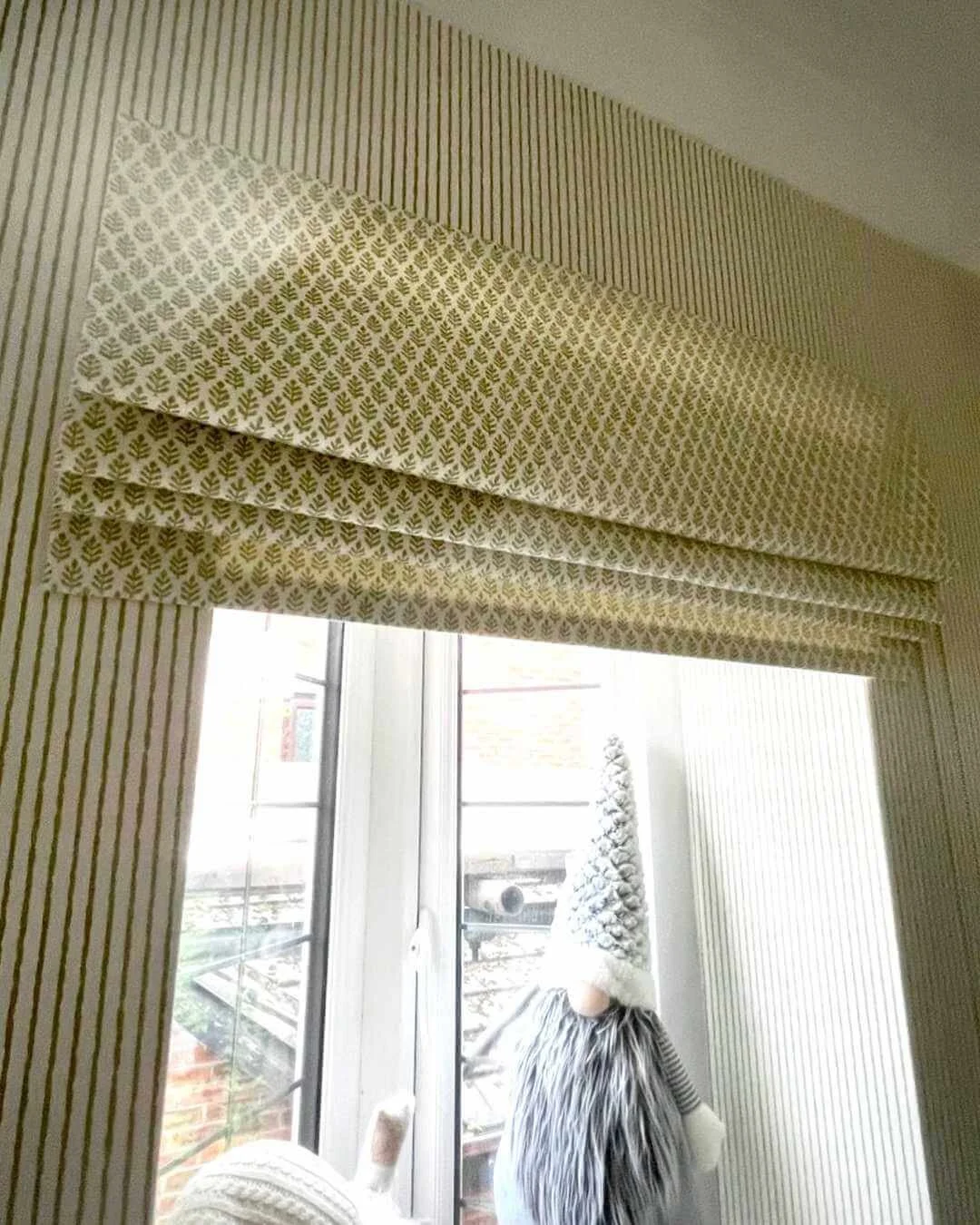 Window with a patterned bespoke roman blind and vertical striped The Pure Edit wallpaper