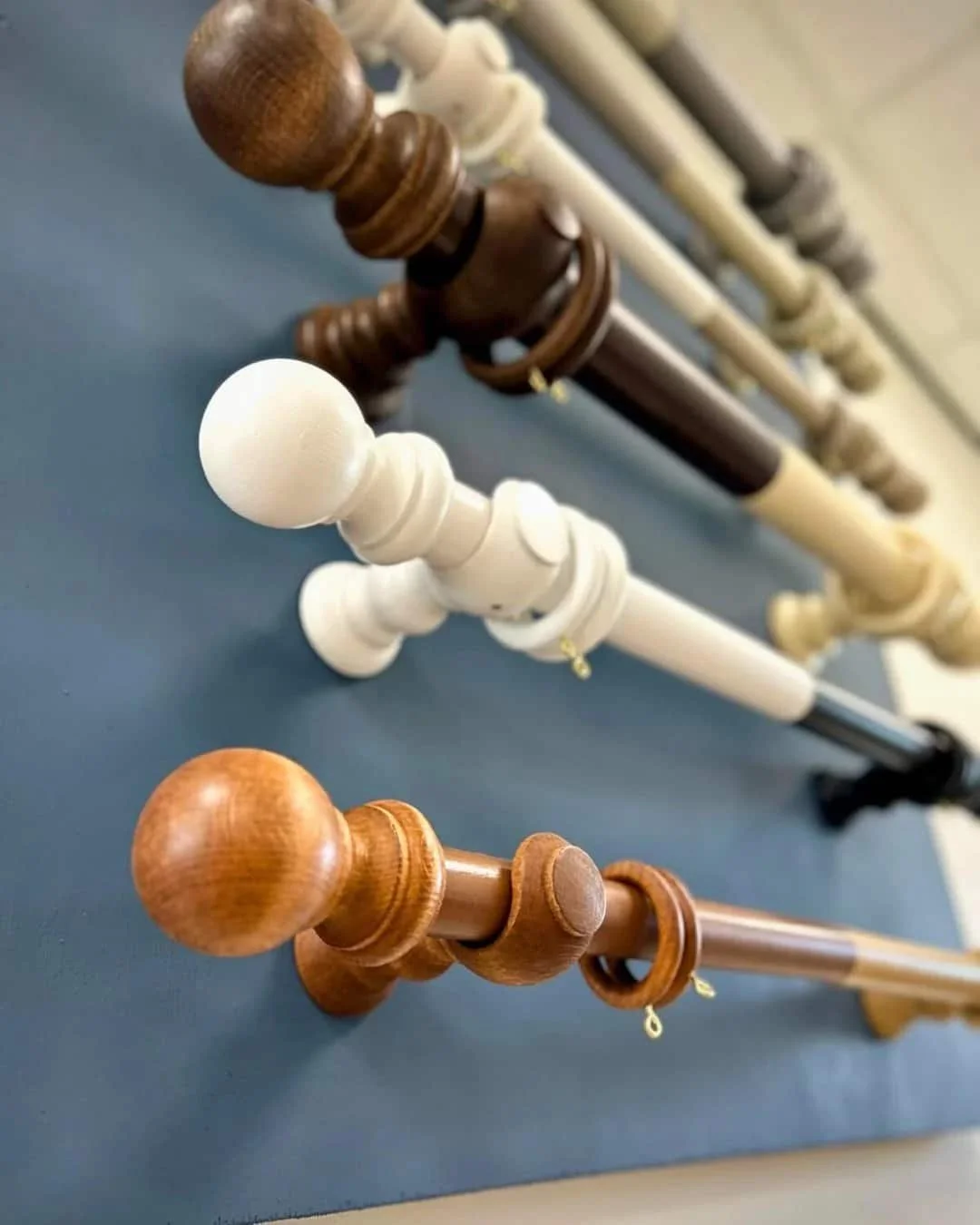 Various wooden curtain rods with different finishes and finials displayed on a wall in the Aconite Interiors showroom