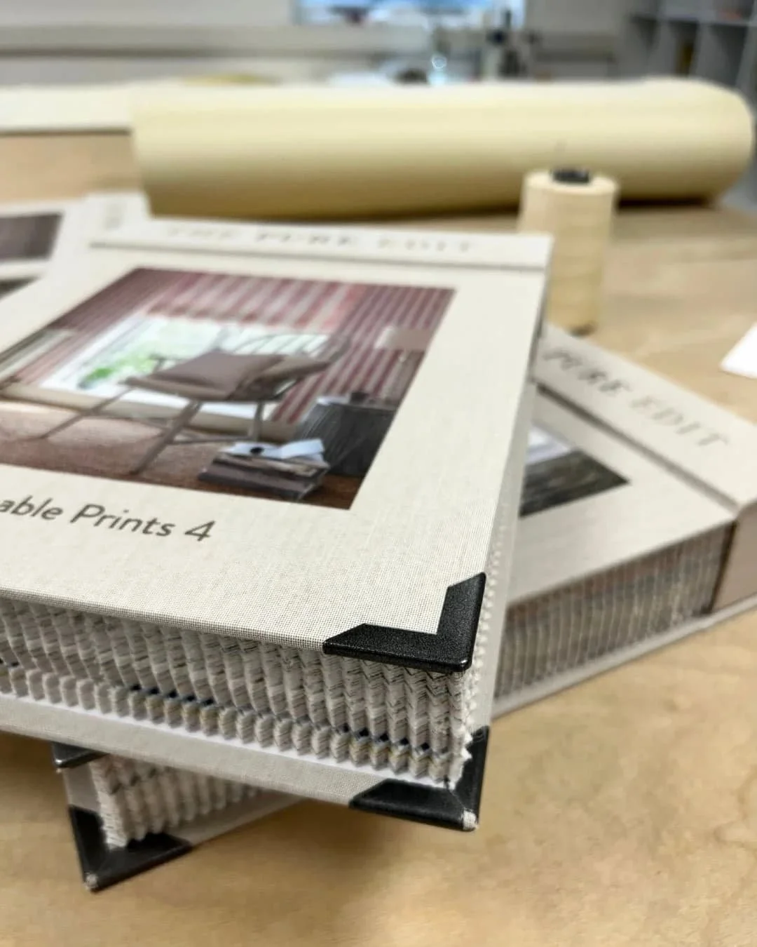 A stack of beige The Pure Edit sample books on a wooden sewing table at the Aconite Interiors workshop Clitheroe