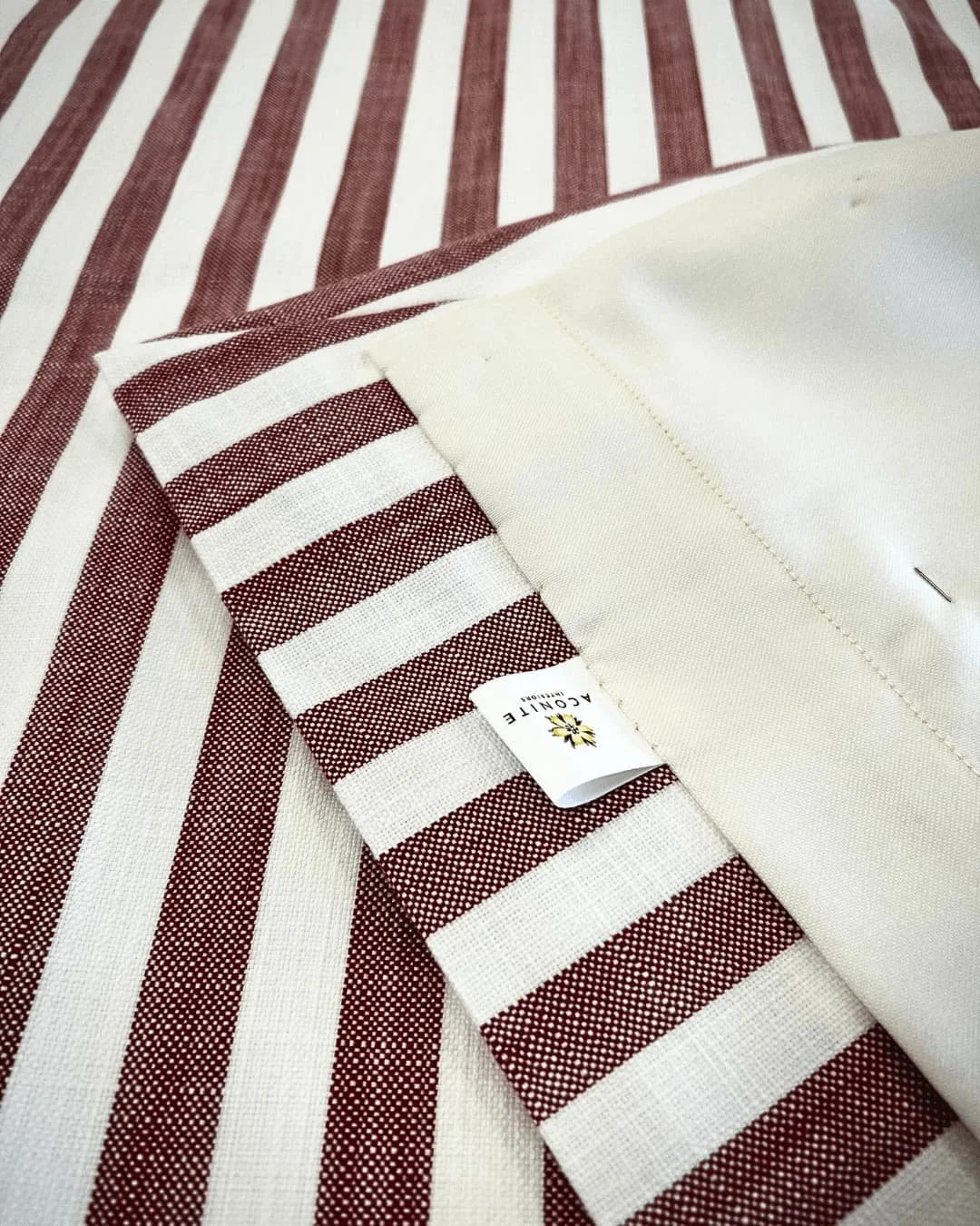 Folded back corner of a red and white stripey curtain to expose the cream lining and Aconite Interiors care label