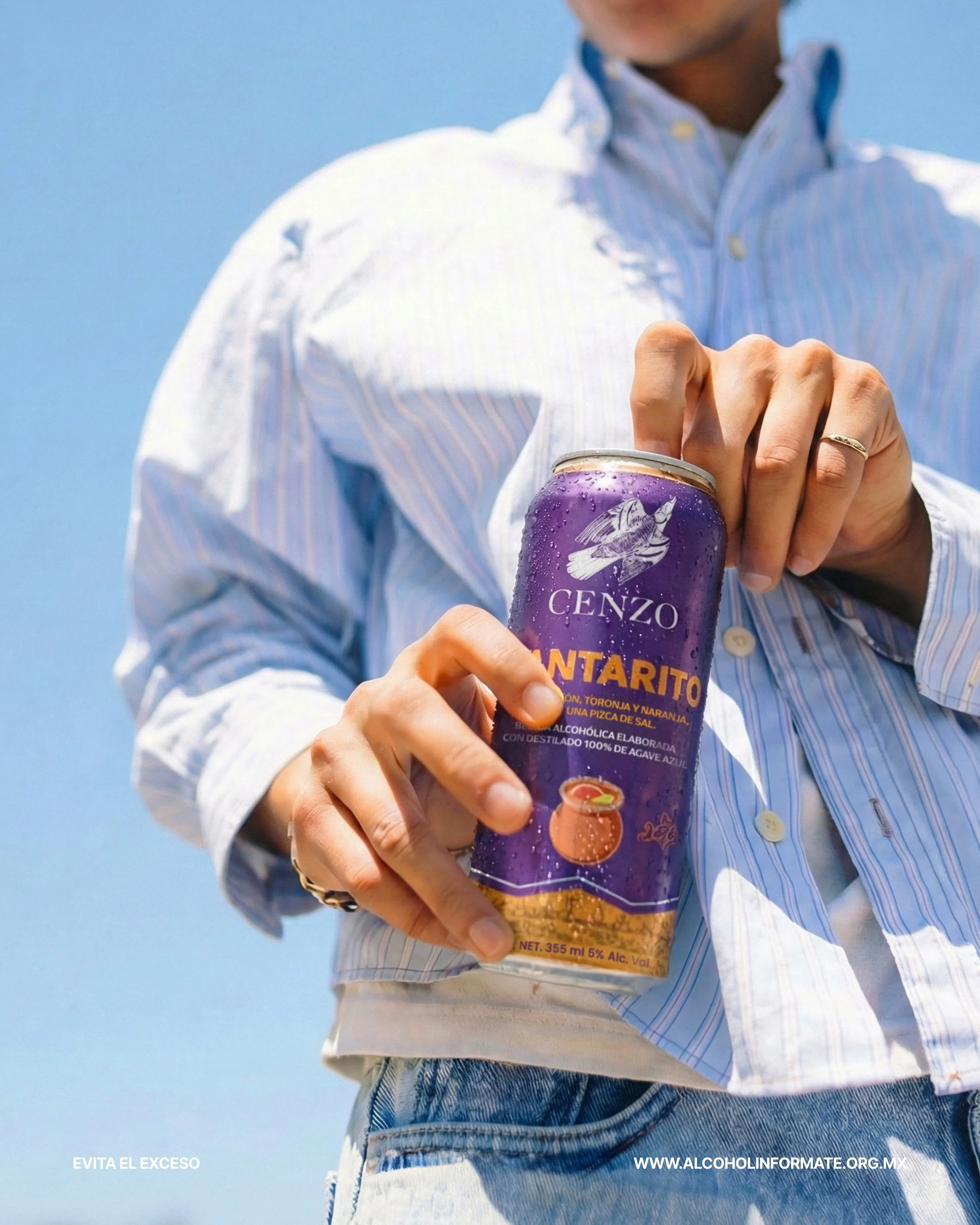 Persona sosteniendo una lata de CENZO SANTARITO con sabor a toronja y naranja, con fondo de cielo azul
