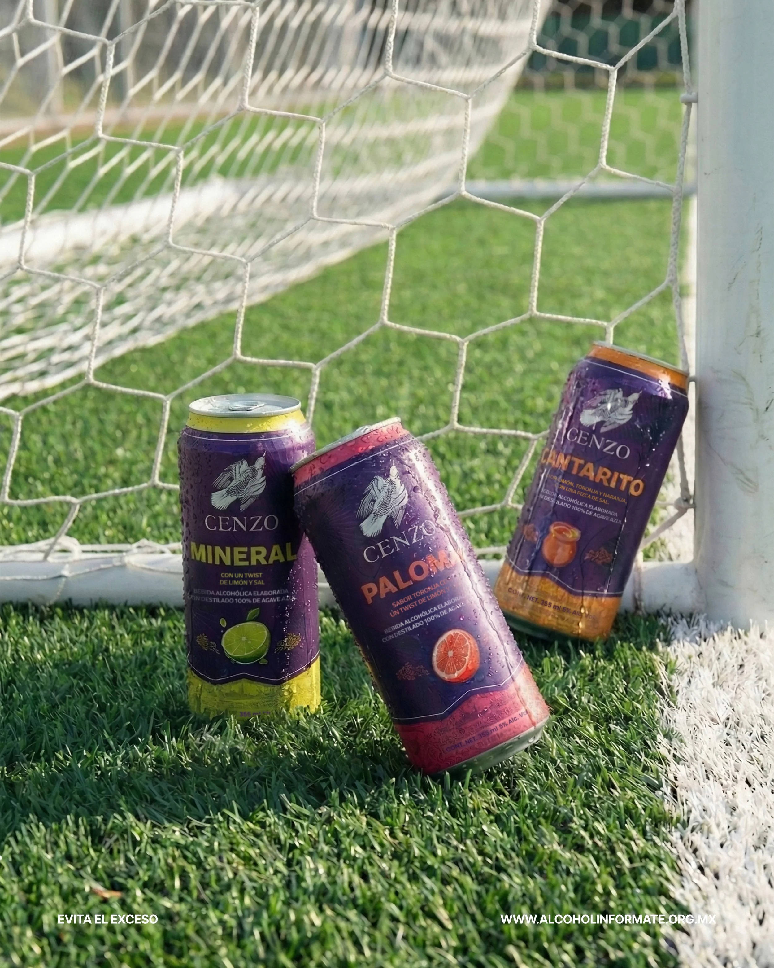 Tres latas de bebidas alcohólicas de la marca Cenzo, una de sabor mineral, otra de sabor paloma y una tercera de sabor cantarito, colocadas en el césped en frente de una portería de fútbol.