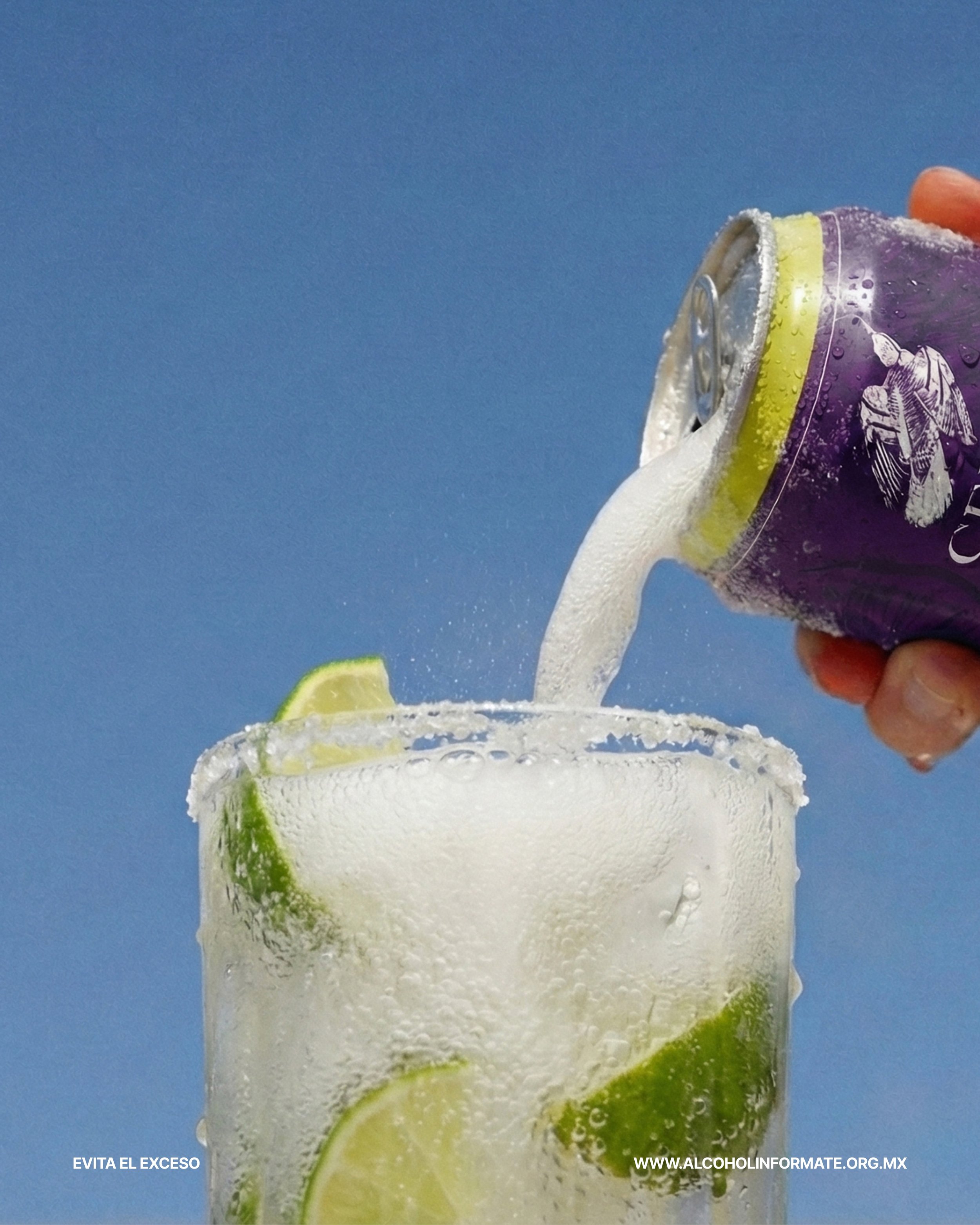 Una mano vierte refresco de soda en un vaso con hielo y rodajas de limón, contra un fondo azul.