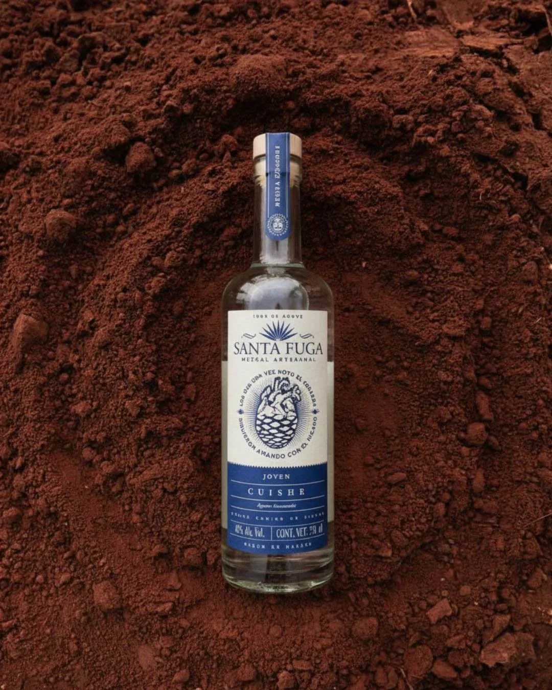 Botella de tequila artesanal Santa Fuga sobre tierra colorada.