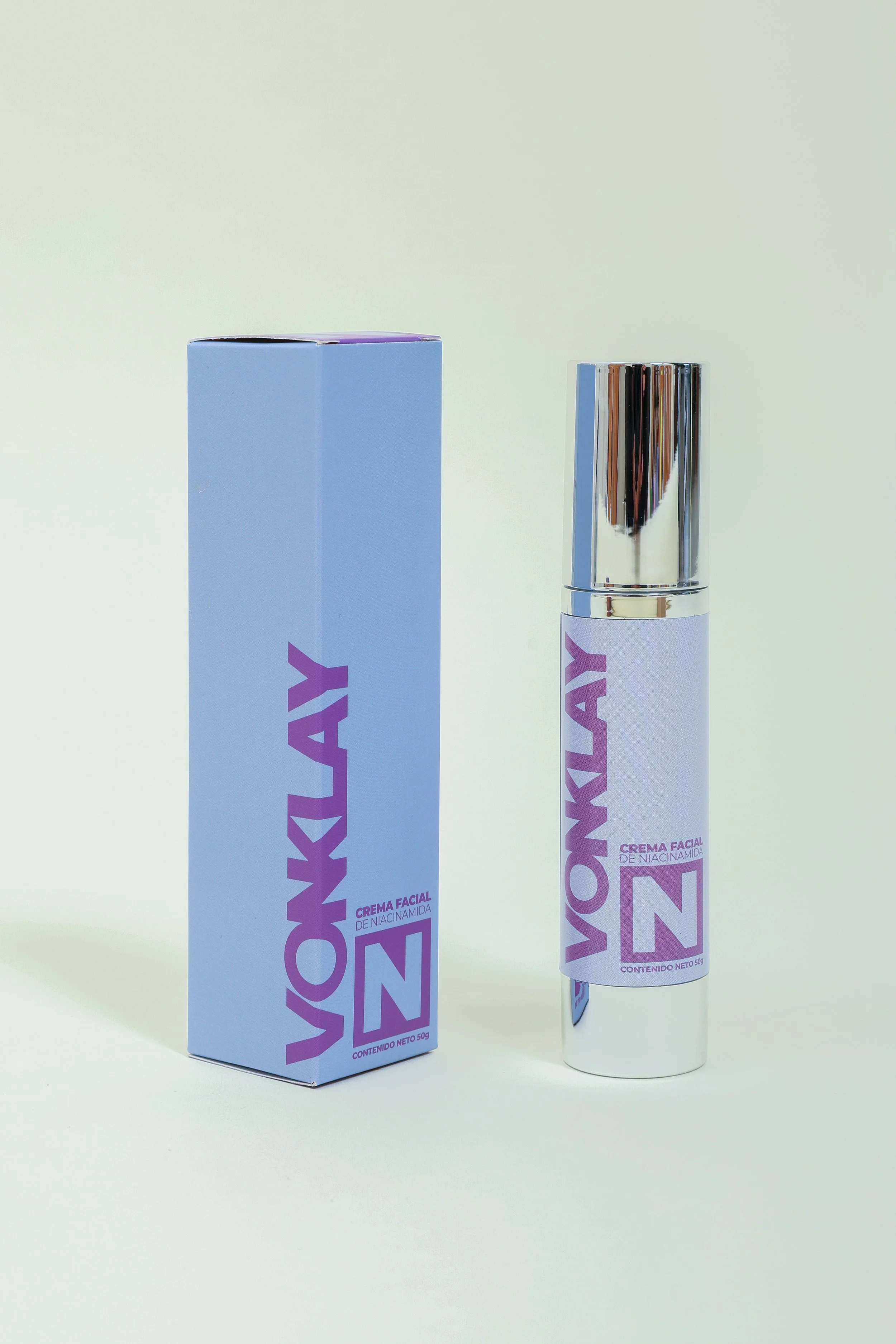 Tubo y caja de crema facial con envase plateado y etiqueta morada con letras grandes que dice 'VOYLAY'