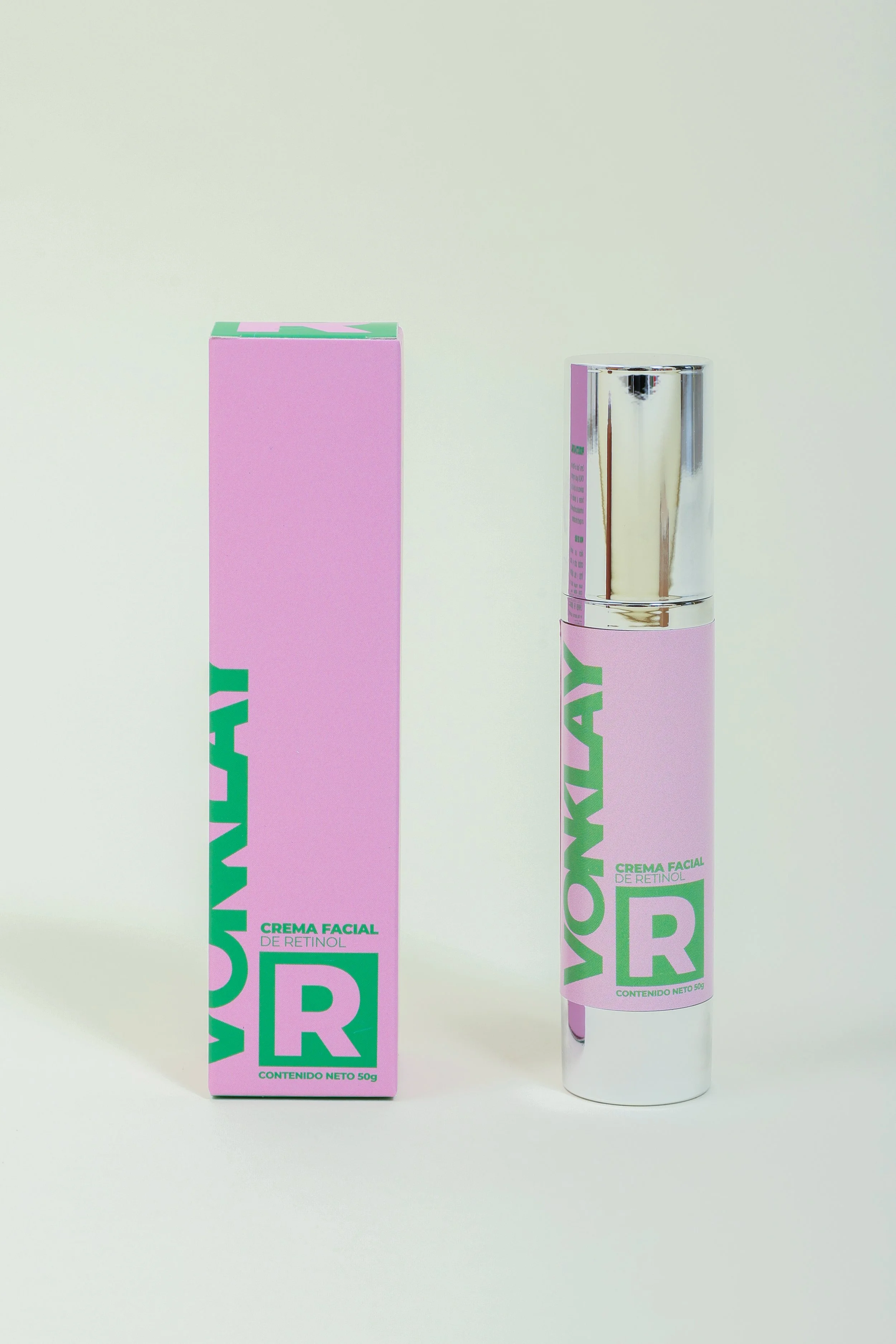 Botella y caja de crema facial de color rosa con etiquetas verdes y letras grandes, con estilo moderno y de diseño limpio.