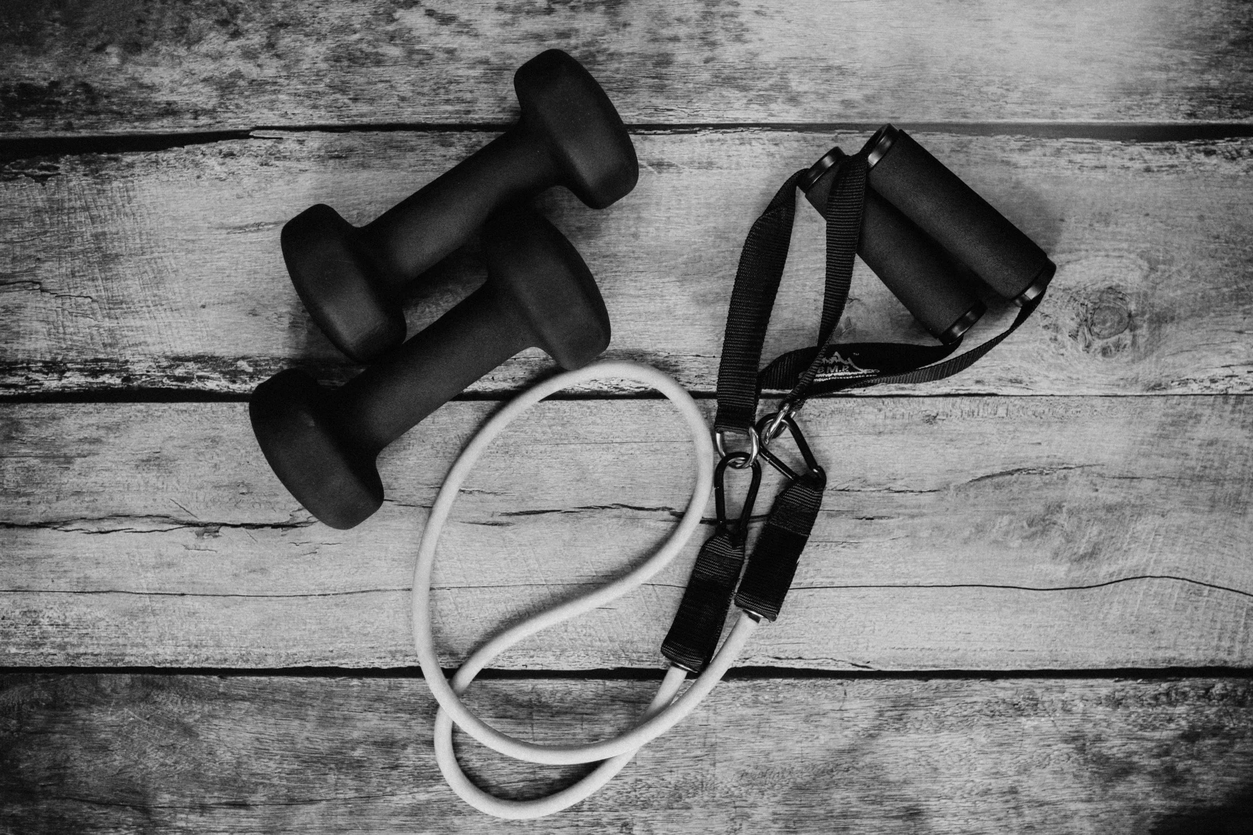 A pair of black dumbbells and an orange resistance band on a wooden floor.