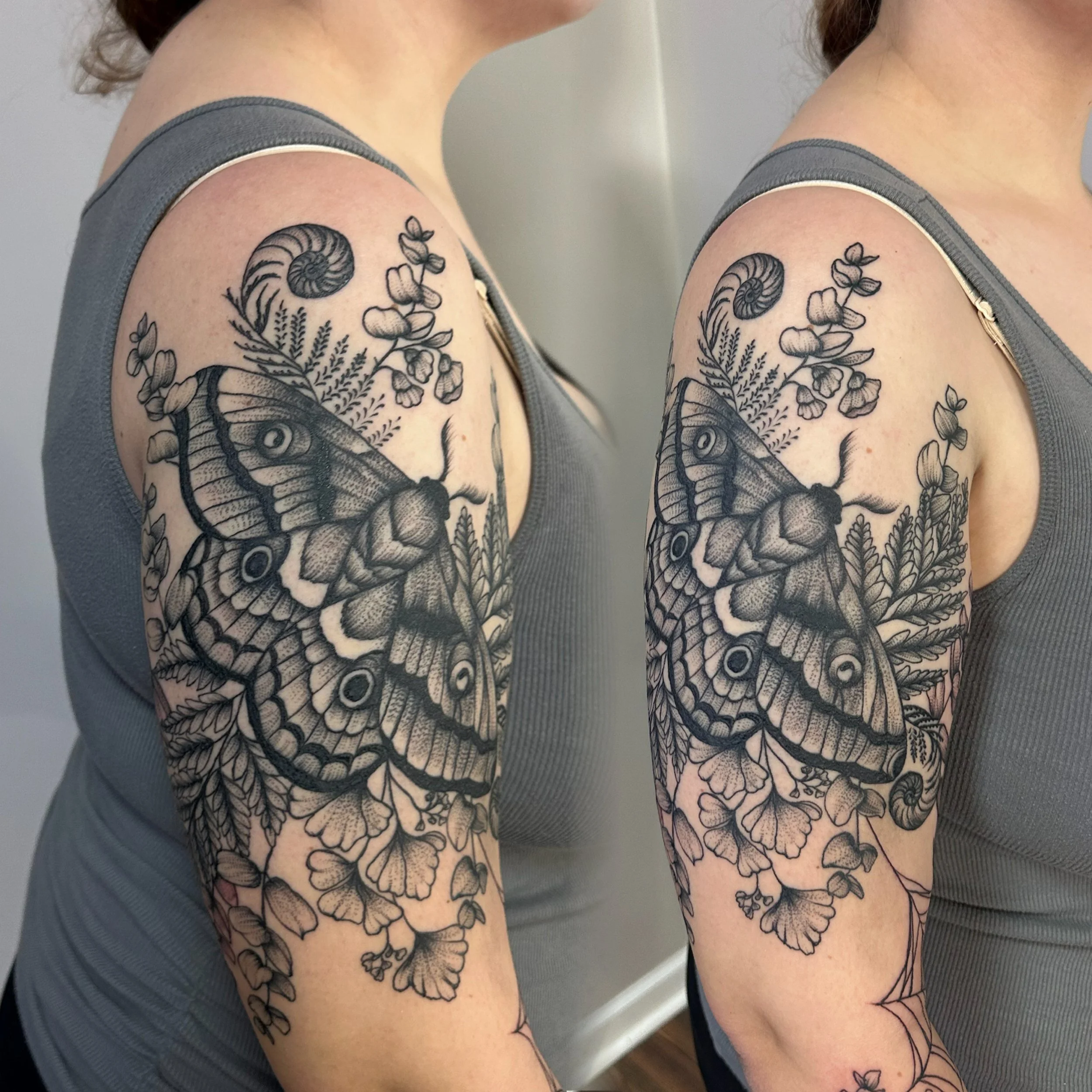 Observe this blackwork masterful moth surrounded by floral decor, wrapping around the upper arm with delicate grace.