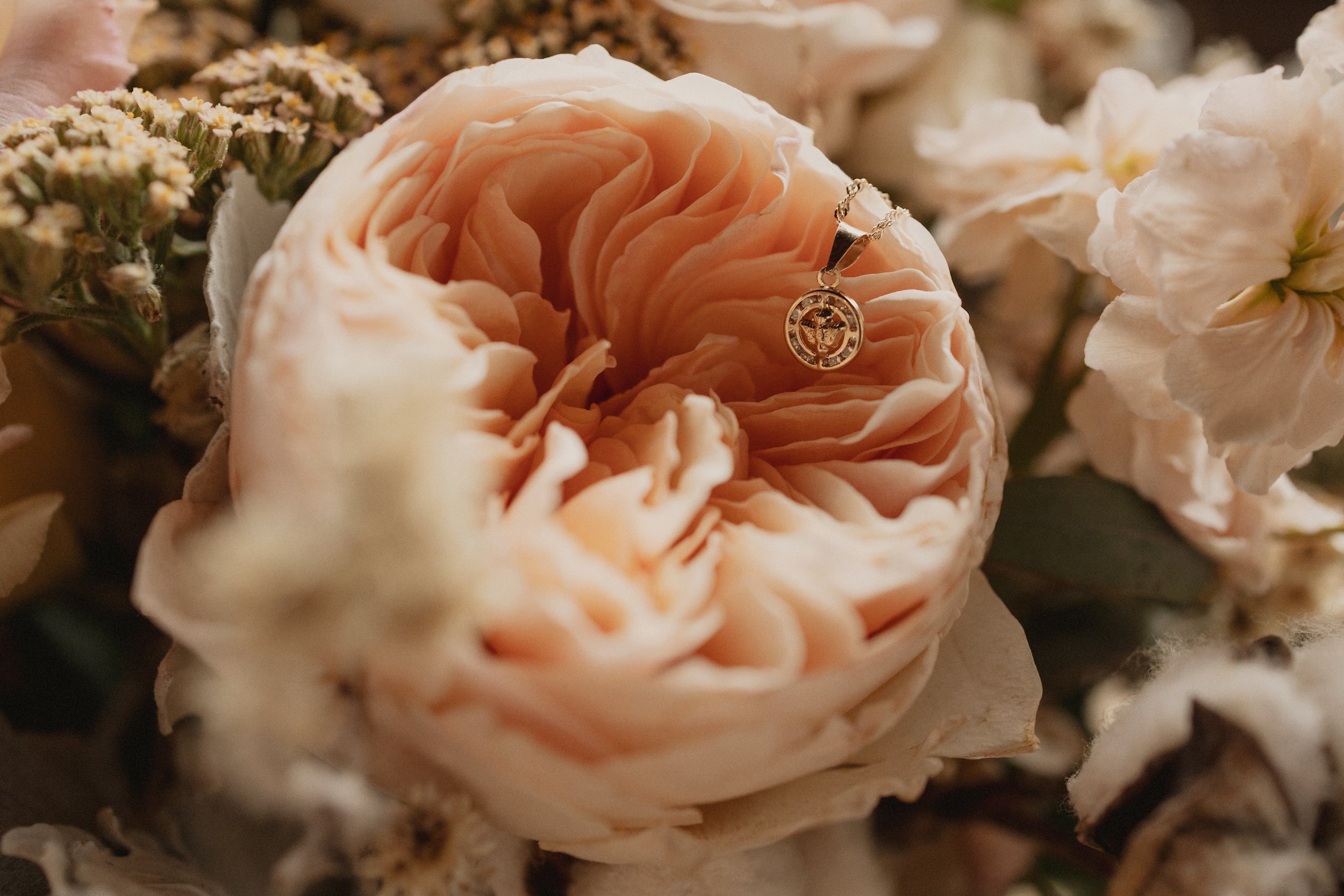 Elegant indoor event space decorated with abundant white and cream floral arrangements hanging from the ceiling and arranged on tables, illuminated by warm candlelight, with a stage or dance floor at the center.