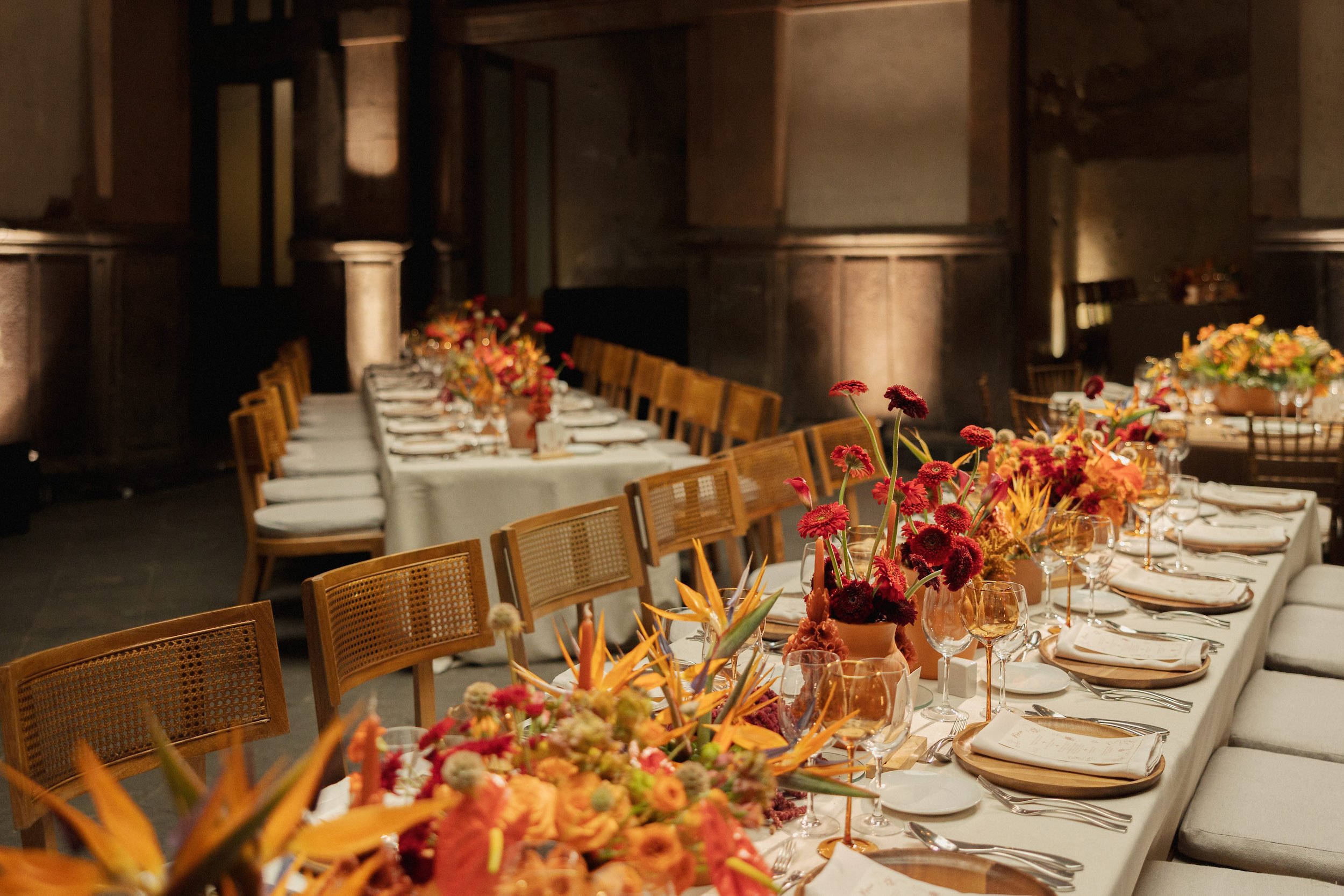 Elegant dining table set with floral centerpieces, glassware, and napkins in a warmly lit, rustic-style room.