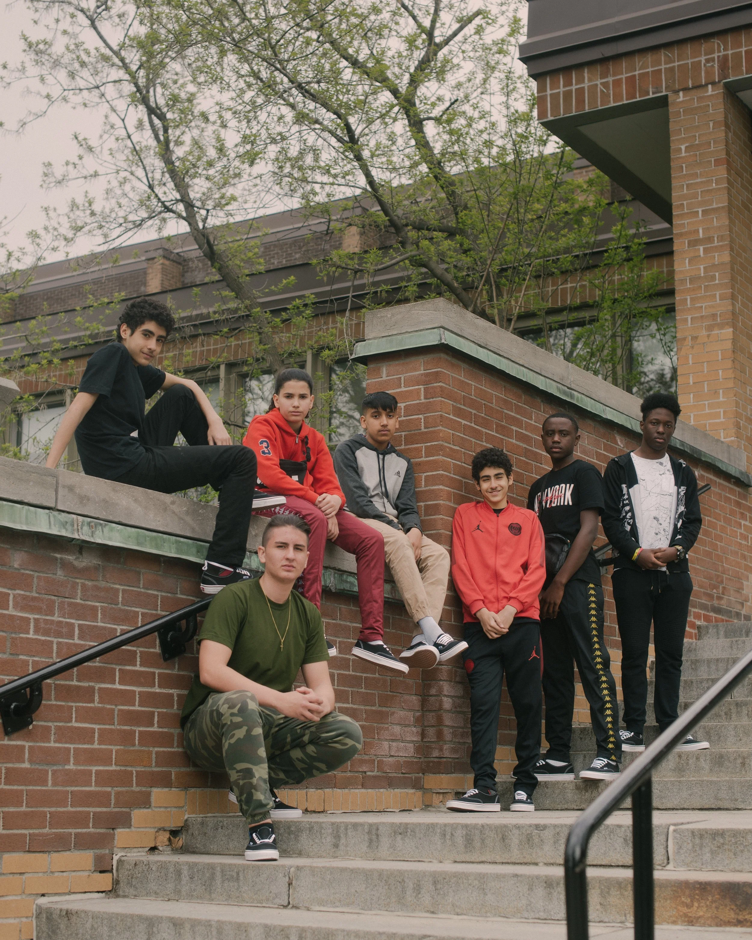 Un groupe de jeunes adolescents posant sur un escalier en pierre devant un mur en briques et un bâtiment, avec des arbres en arrière-plan.