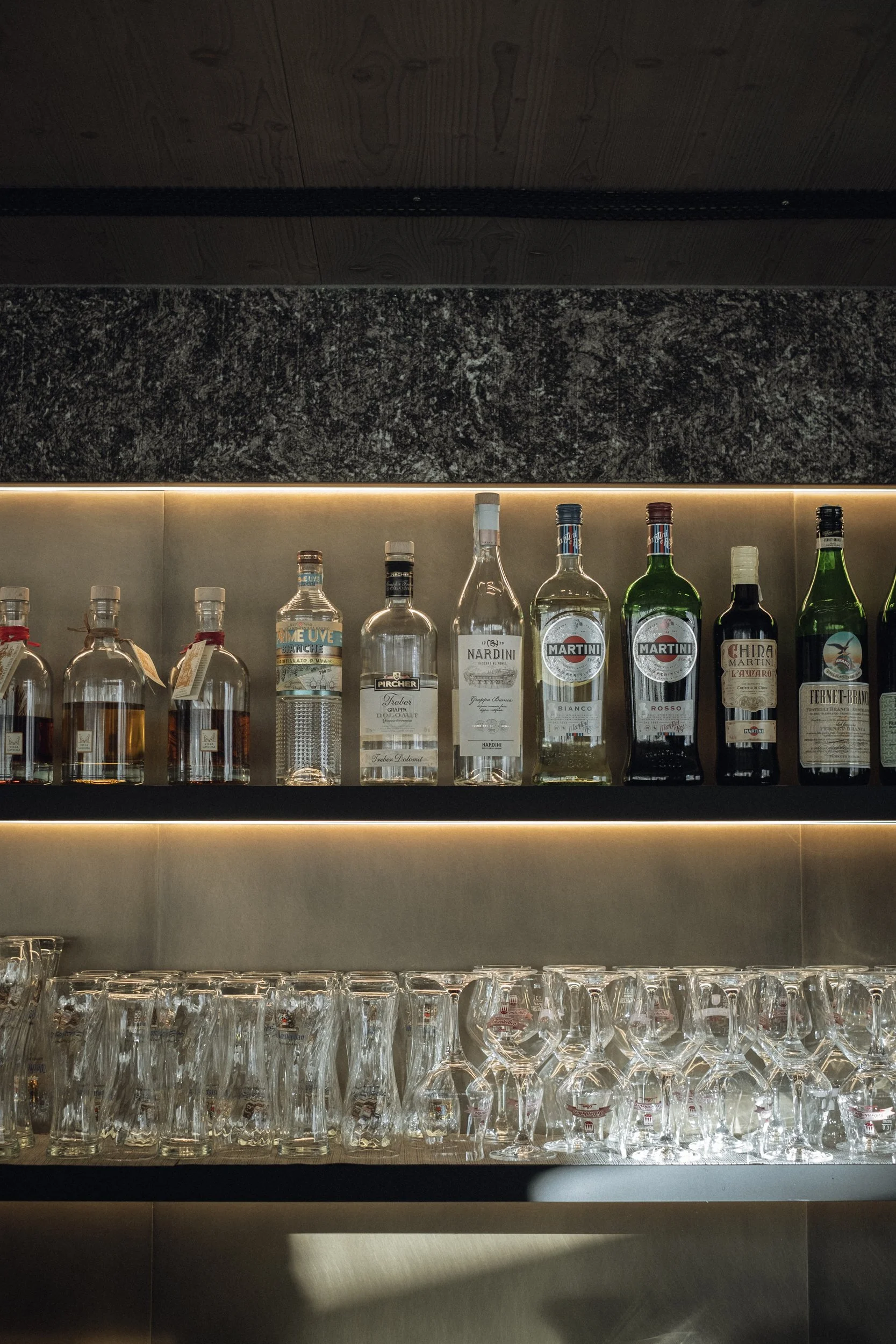 Regal mit verschiedenen Spirituosenflaschen und geordneten Gläsern in einem Barbereich.