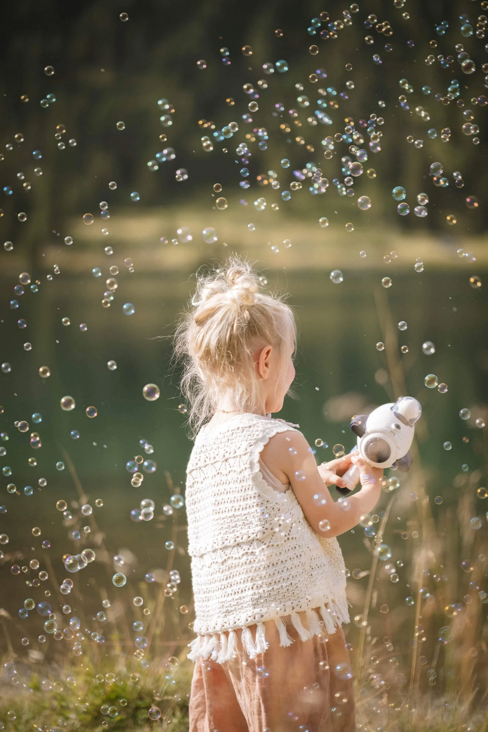 Ein kleines Mädchen im Sommer, das Seifenblasen in der Hand hält und im Freien spielt.