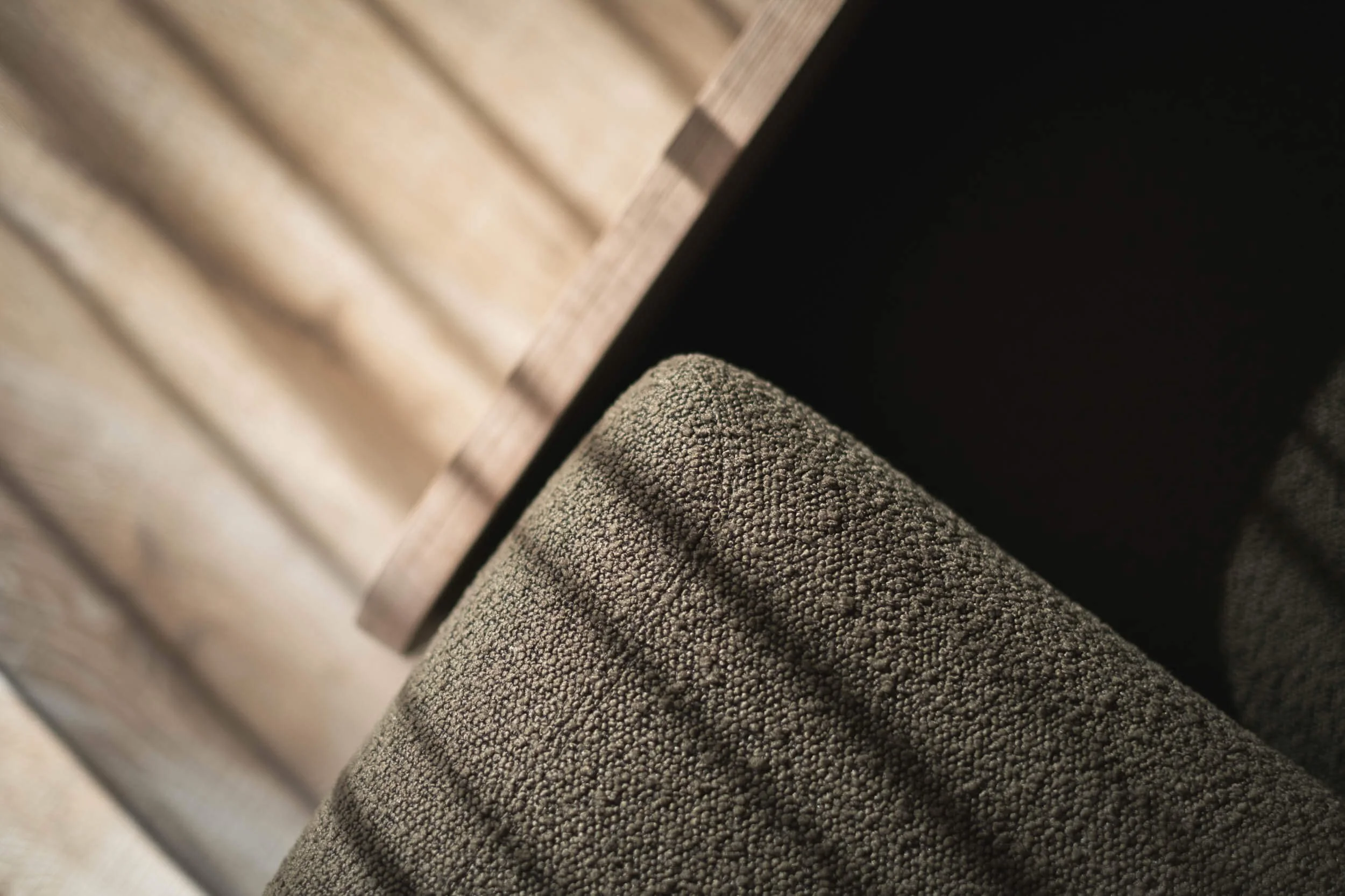 Nahaufnahme eines braunen, texturierten Möbelstücks, vermutlich ein Sesselkissen, vor einem Holztisch.