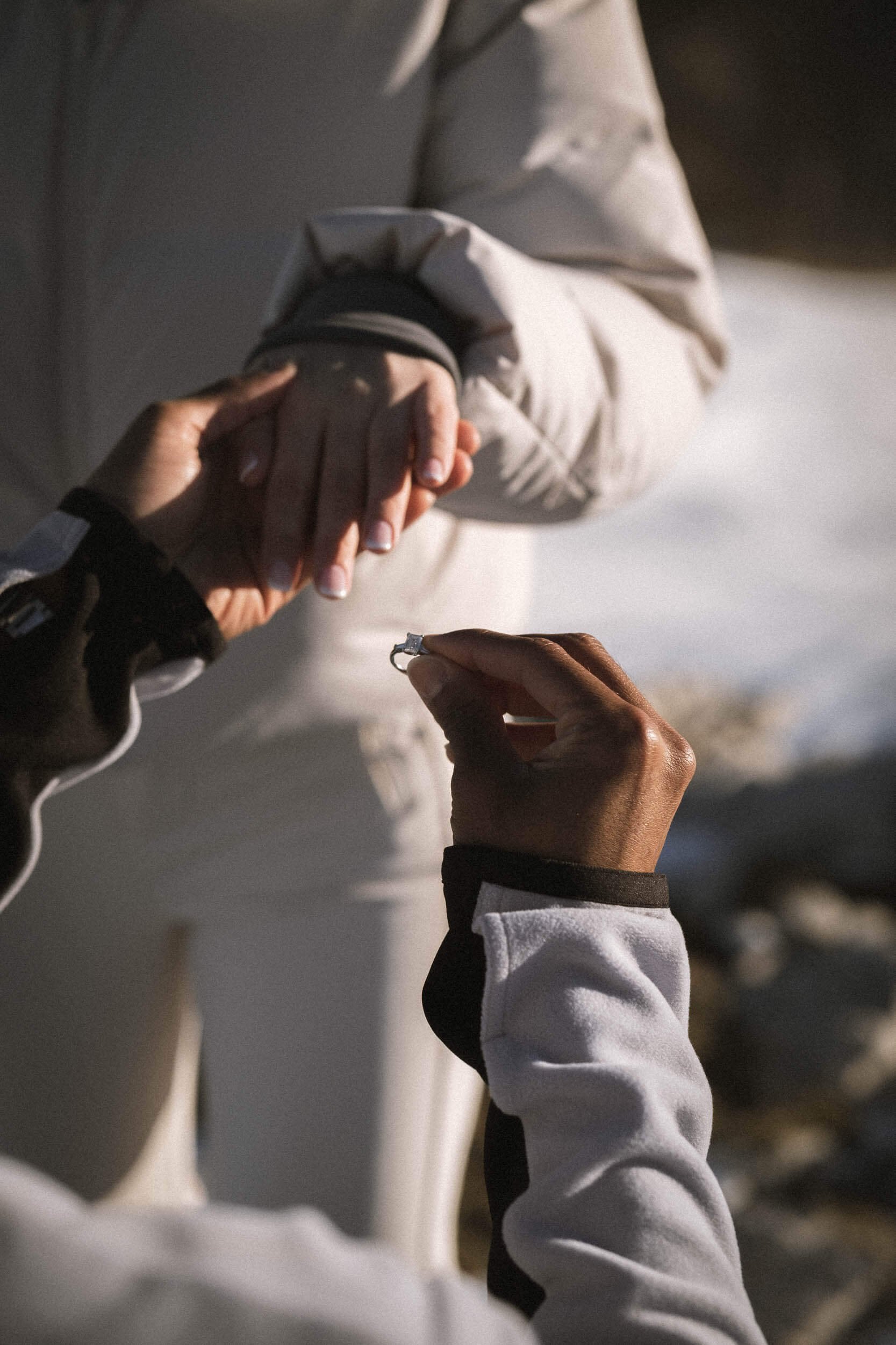 Zwei Menschen, die bei Sonnenuntergang Hände halten, eine Person reicht der anderen einen Ring.