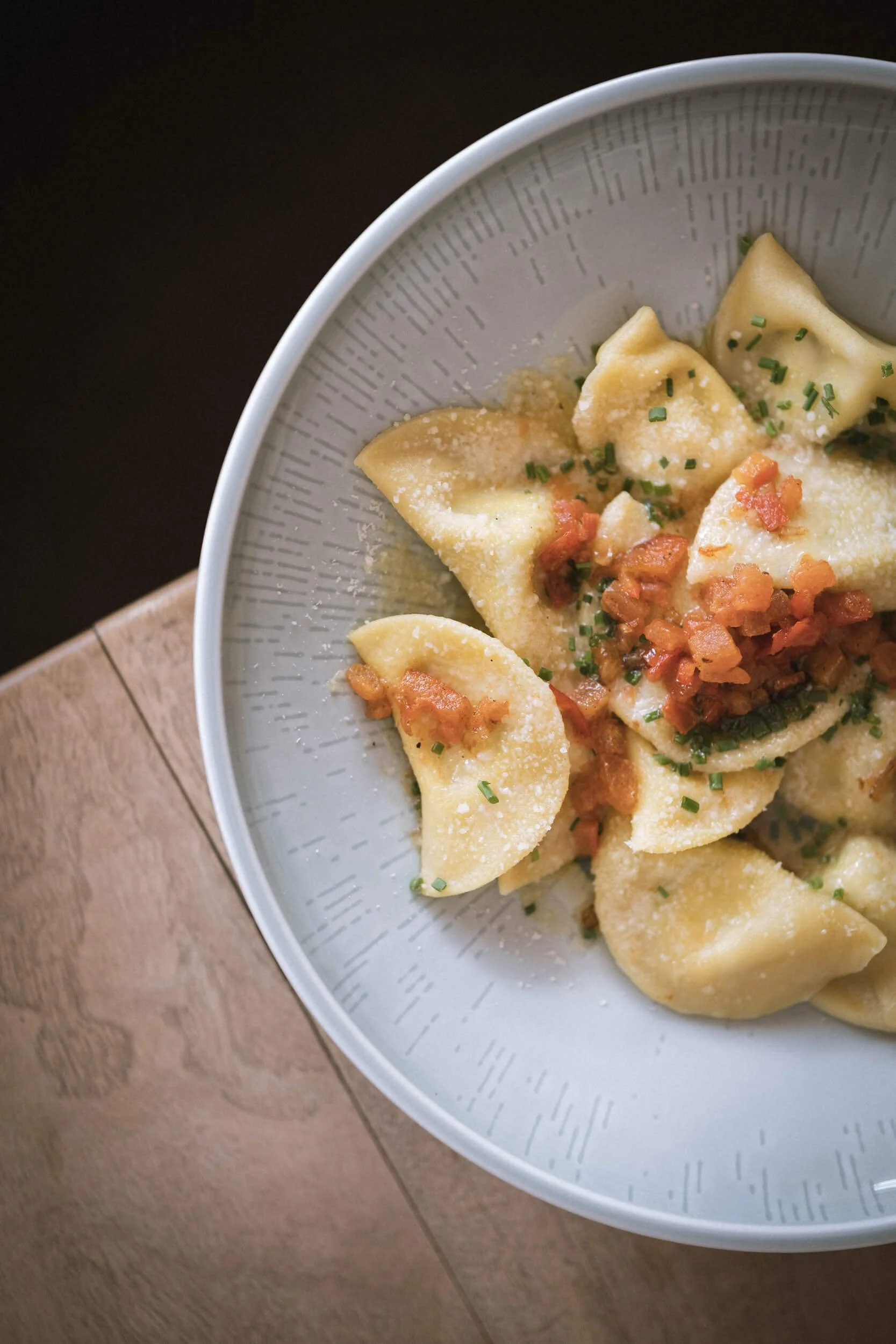 Frische hausgemachte Ravioli mit Speck und Parmesan in einer weißen Schüssel, serviert auf einem Holzbrett.