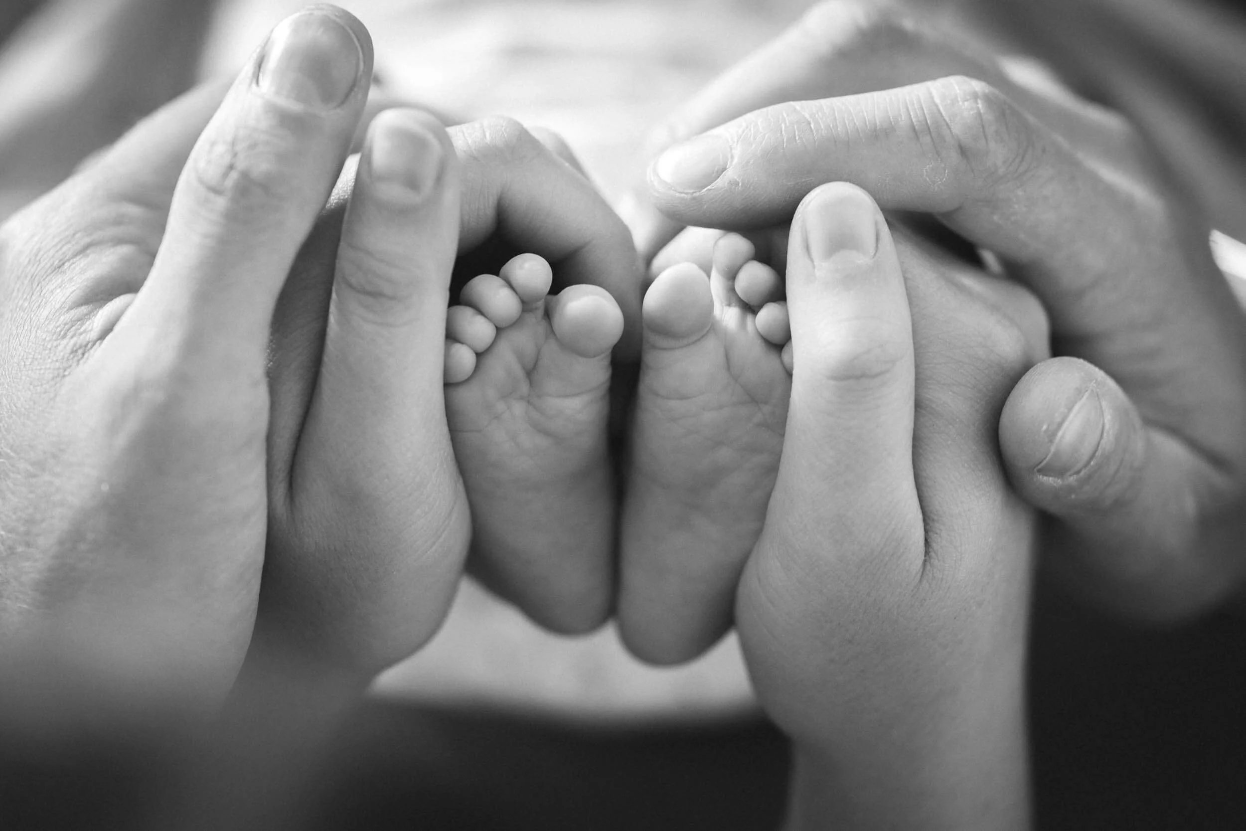 Nahaufnahme von Händen, die ein kleines Baby umarmen, in Schwarz-Weiß.