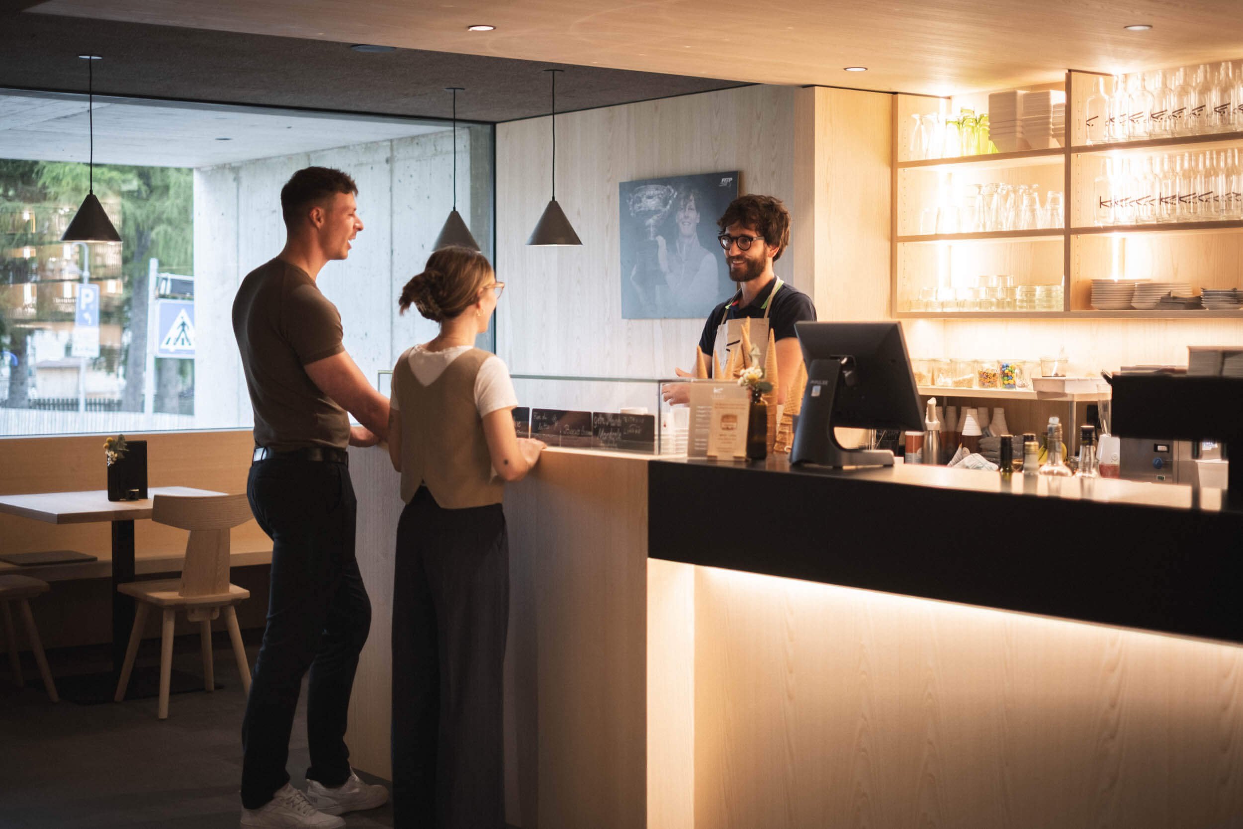 Drei Personen im Café, ein Mann und eine Frau sprechen mit einem Barista am Café-Theke.