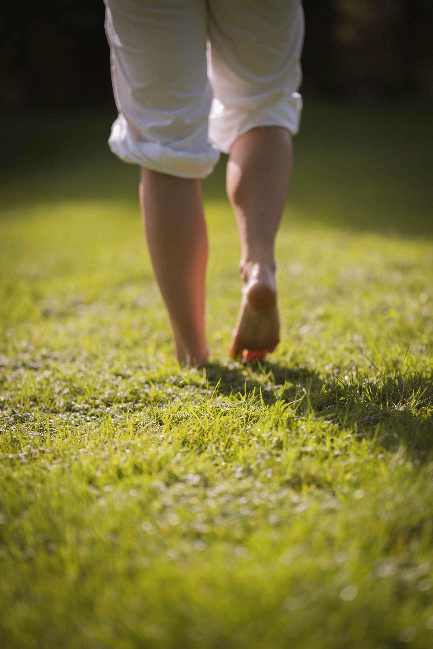 Nahaufnahme von nackten Beinen und Füßen einer Person beim Barfußlaufen auf grünem Gras im Freien
