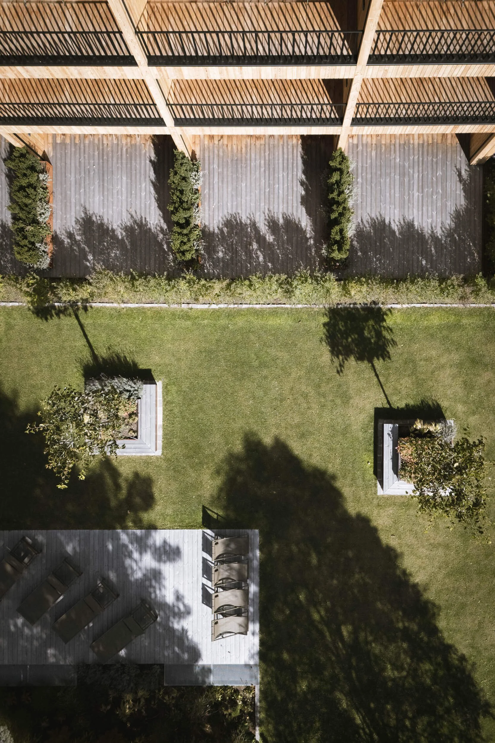 Ansicht eines Gartens mit Rasen, Bäumen, Pflanzkübeln, Schatten von Bäumen und einem Gebäude mit Balkon