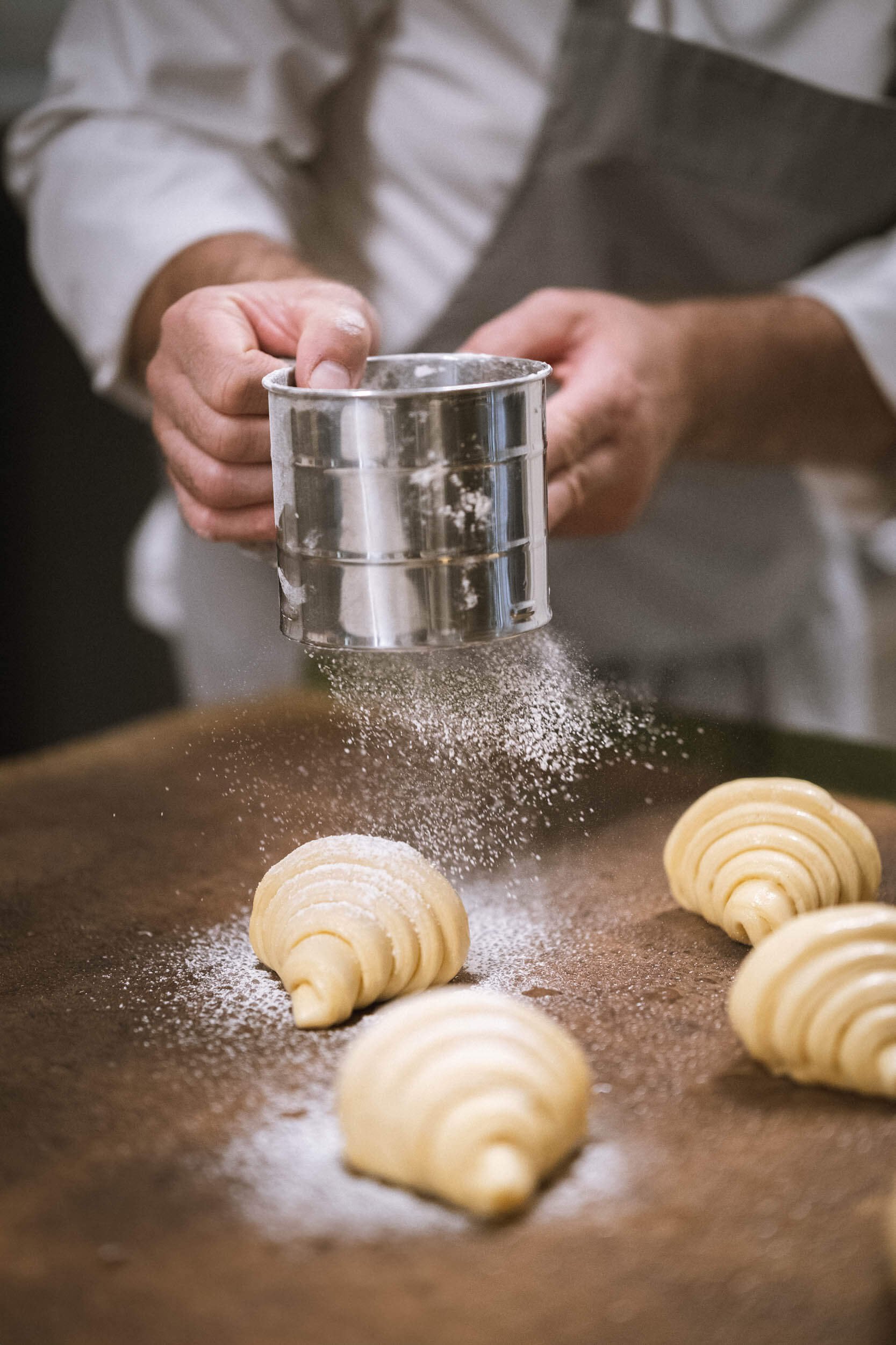 Person bestäubt Croissants mit Mehl auf einem Backbrett.