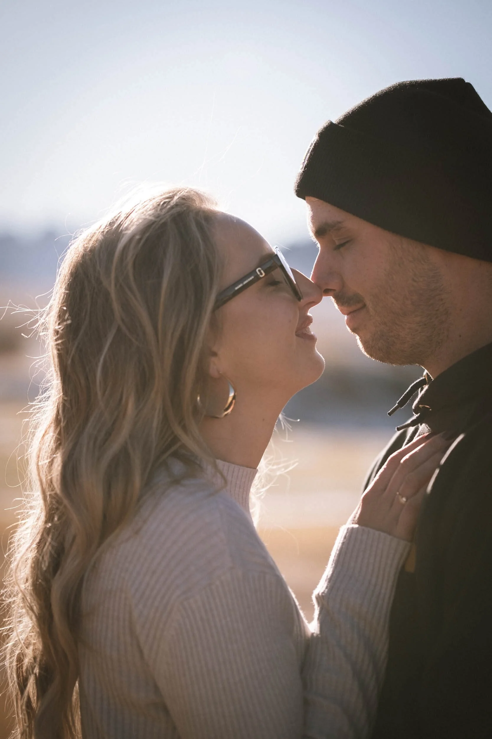 Ein Paar steht sich auf einer sonnigen, offenen Landschaft gegenüber, ihre Nasen berühren sich, ihre Augen sind geschlossen.