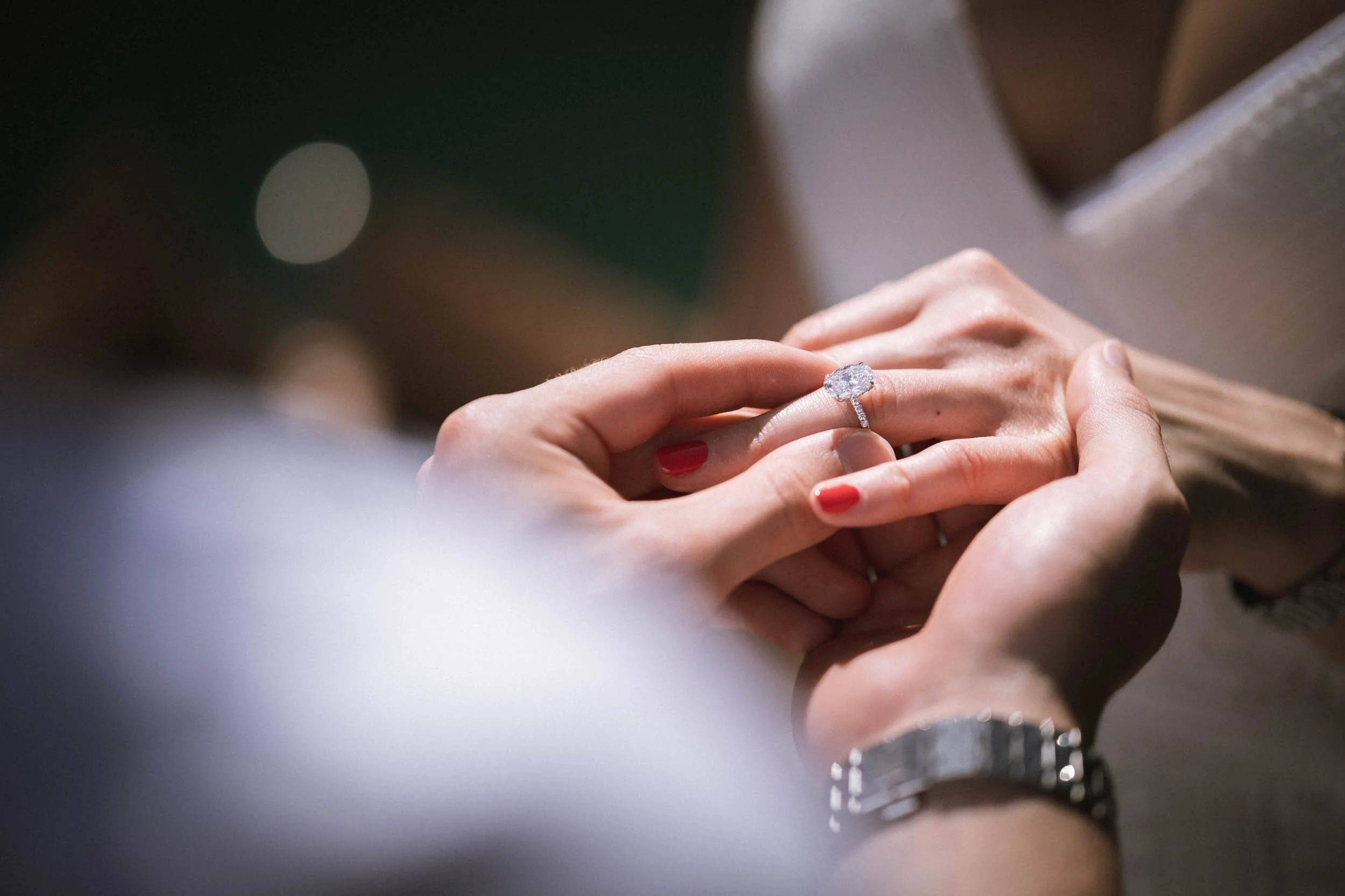 Nahaufnahme einer Hand, die einen Verlobungsring mit einem großen Diamanten trägt, während eine andere Person die Hand hält.