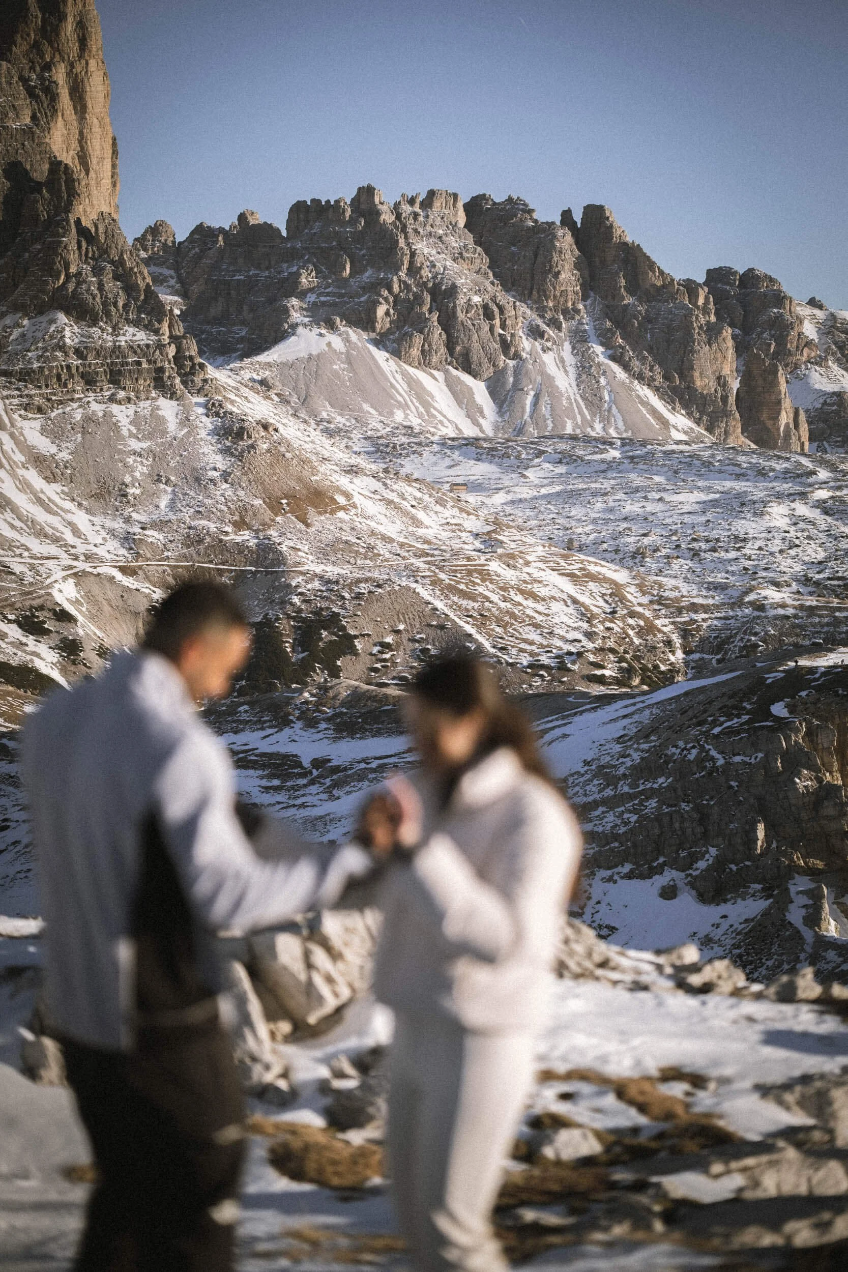 Zwei Menschen in Winterkleidung stehen vor einer schneebedeckten Berglandschaft, bei der das Bild unscharf ist.