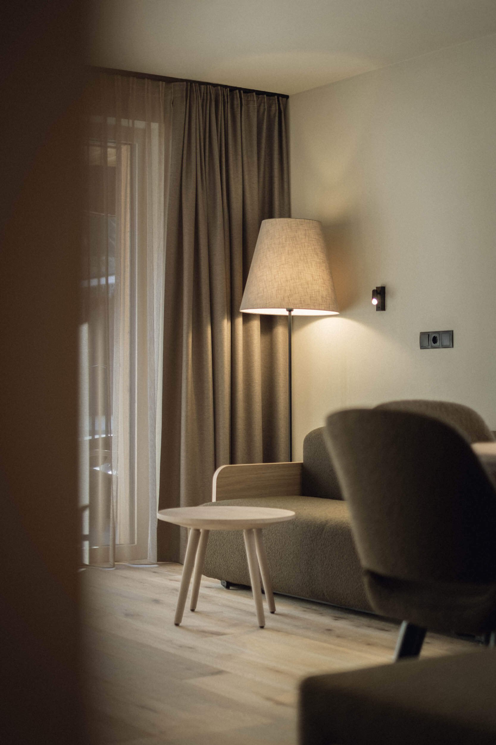 Gemütliches Wohnzimmer mit Stehlampe, Sofa, Sitzstuhl, Nachdenklich- und Vorhänge, Holzboden.