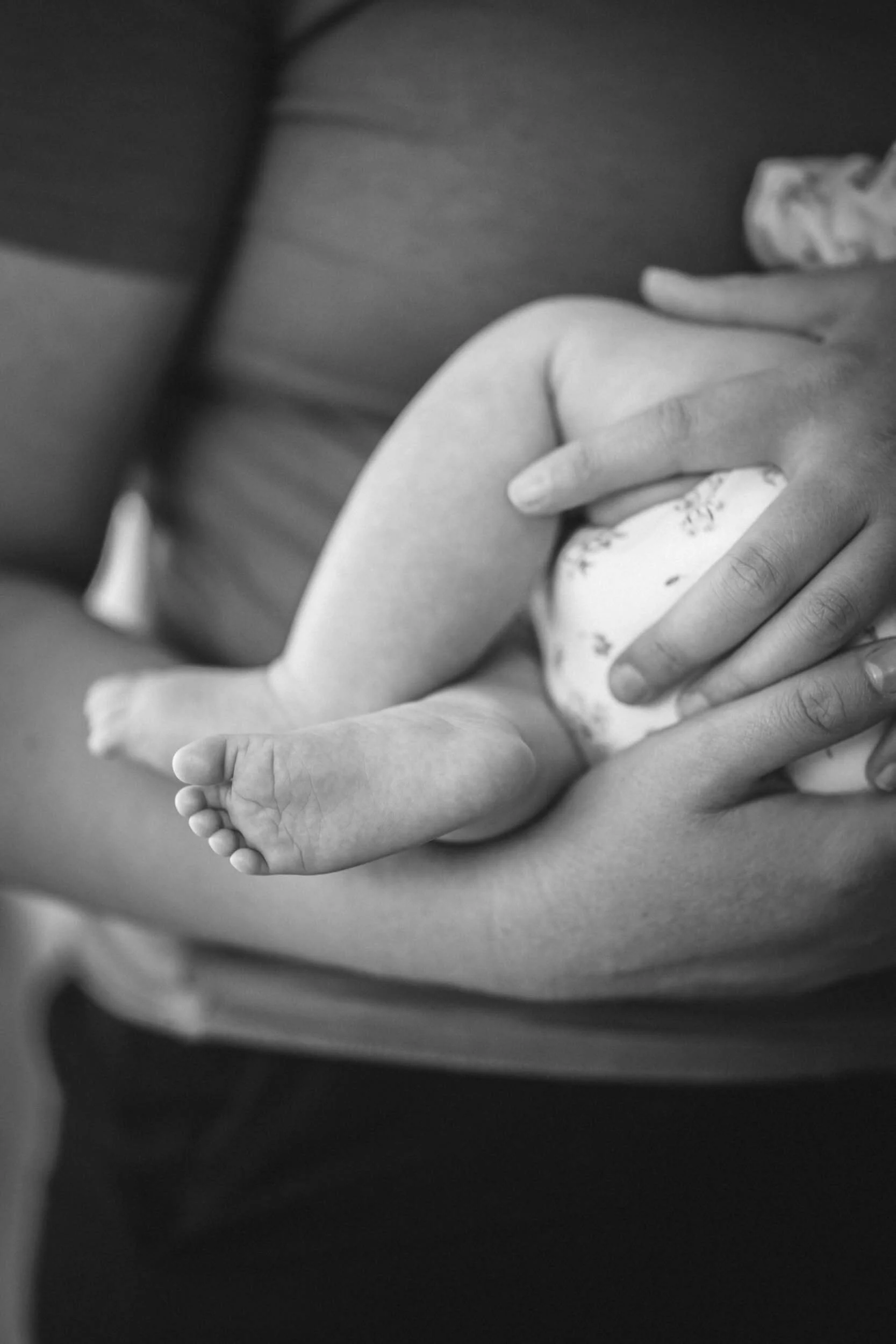 Nahaufnahme eines Babys, das auf einer Person liegt, die es hält. Das Bild ist in Schwarz-Weiß.