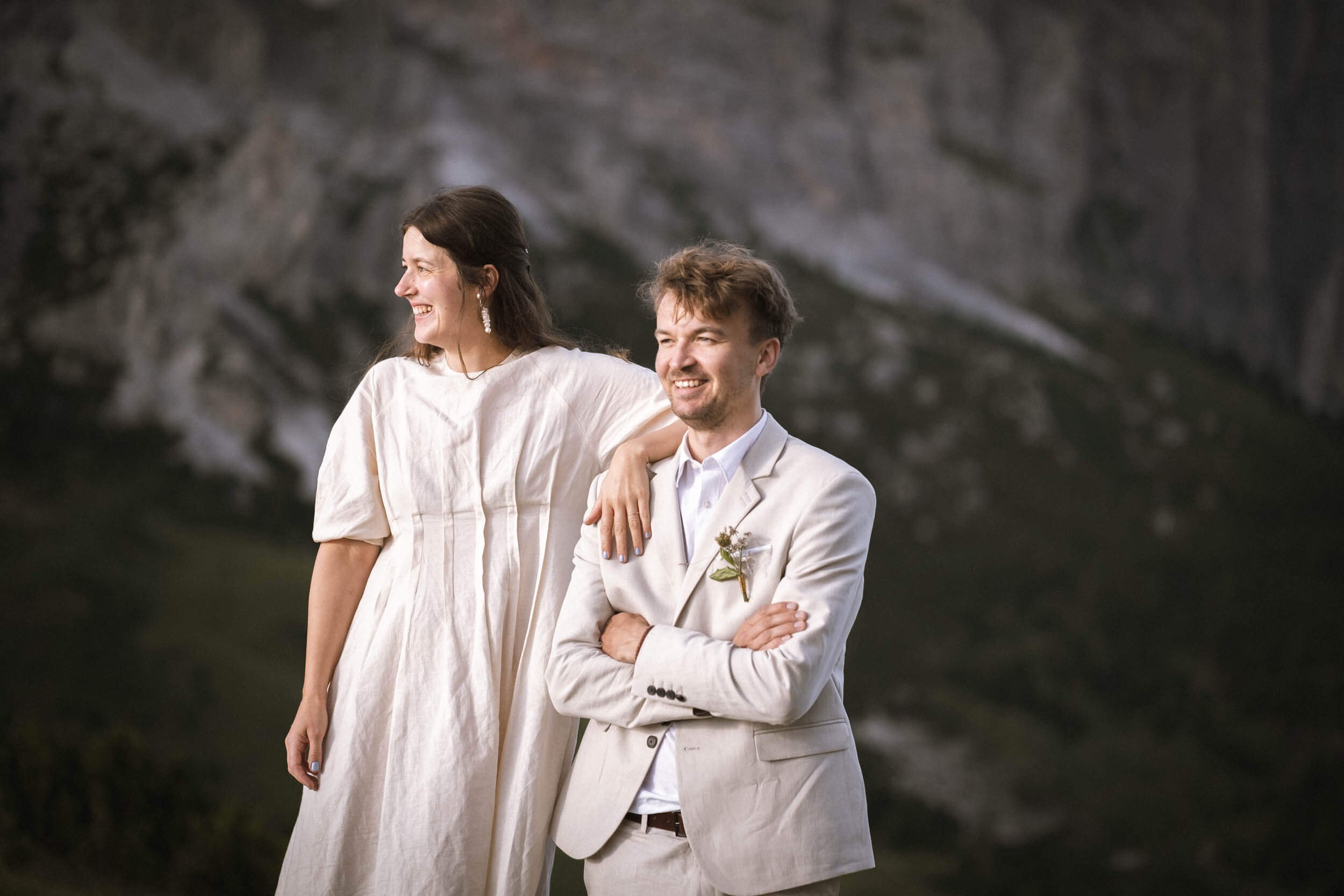 Ein lachendes Paar in formeller Kleidung vor einer natürlichen Kulisse, wahrscheinlich bei einer Hochzeit oder einem besonderen Anlass.