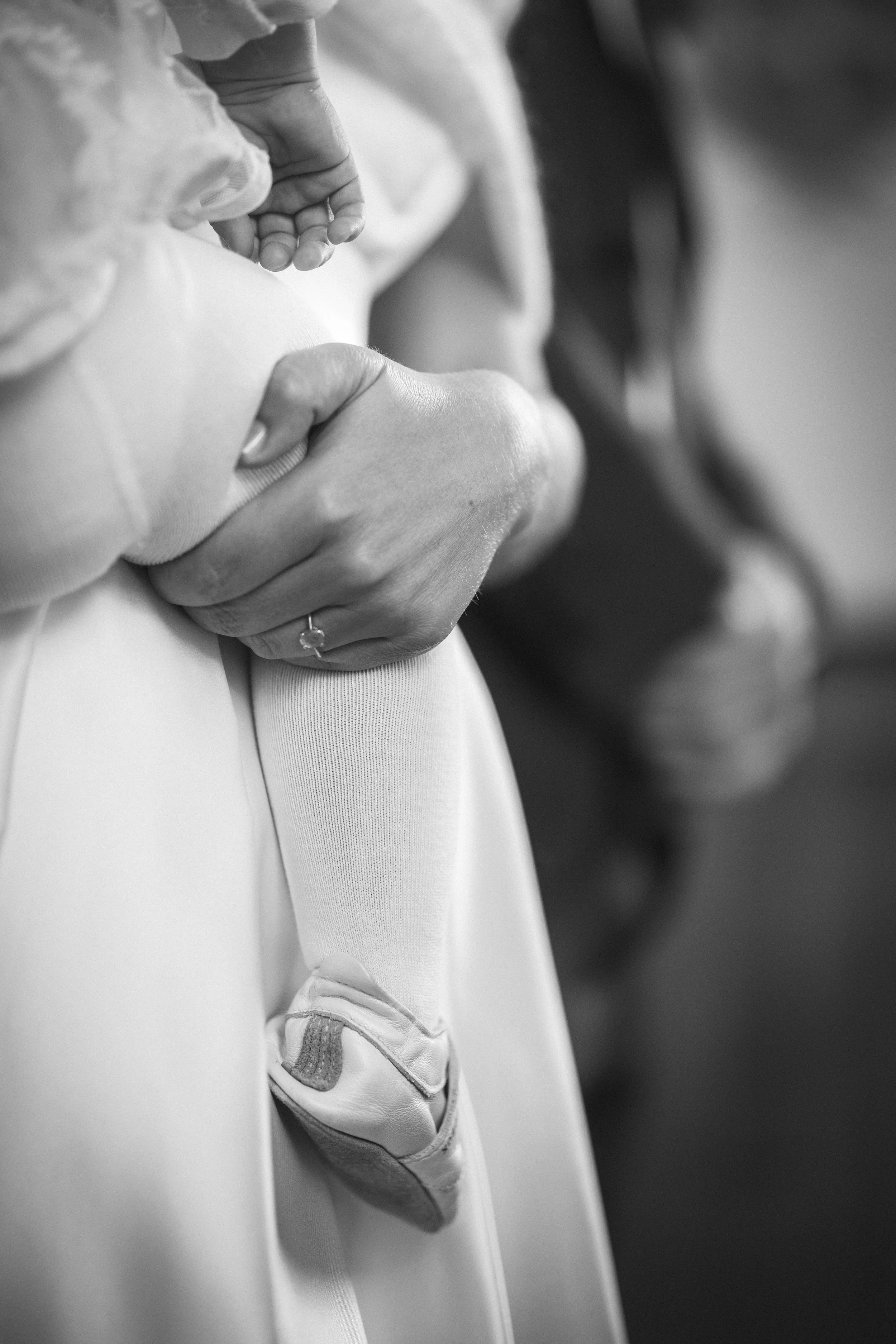 Ein Erwachsener hält die Hand eines Babys, die in einem Handschuh steckt, im Schwarz-Weiß. Die Szene symbolisiert Fürsorge und Verbundenheit.