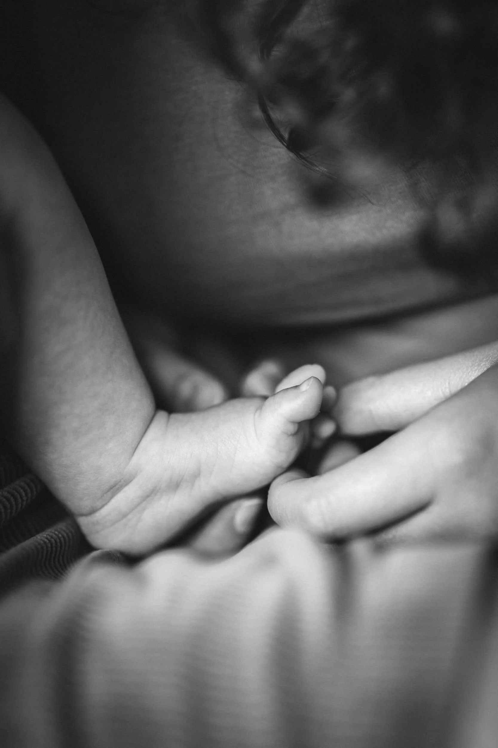 Eine Nahaufnahme eines Erwachsenen und eines Babys, die sich an den Händen halten, in Schwarz-Weiß.