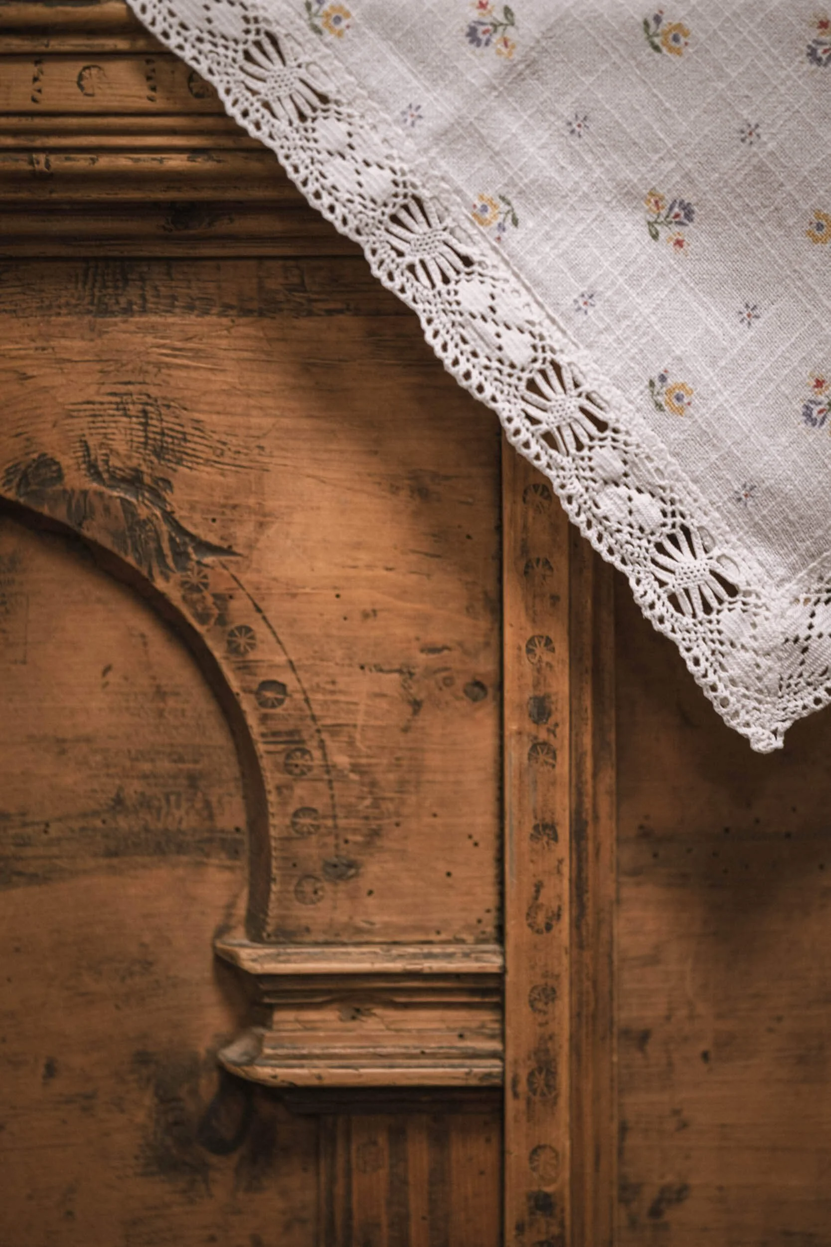 Ein holzfarbener Tisch mit einer weißen Tischdecke mit Stickereien und Spitze. Die Tischdecke liegt teilweise auf dem Tisch.
