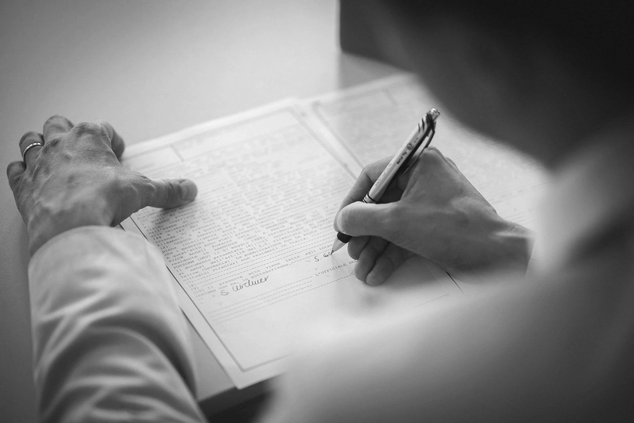 Schwarz-weiße Aufnahme einer Person, die einen Blick auf ein Dokument hat und es mit einem Kugelschreiber unterschreibt.