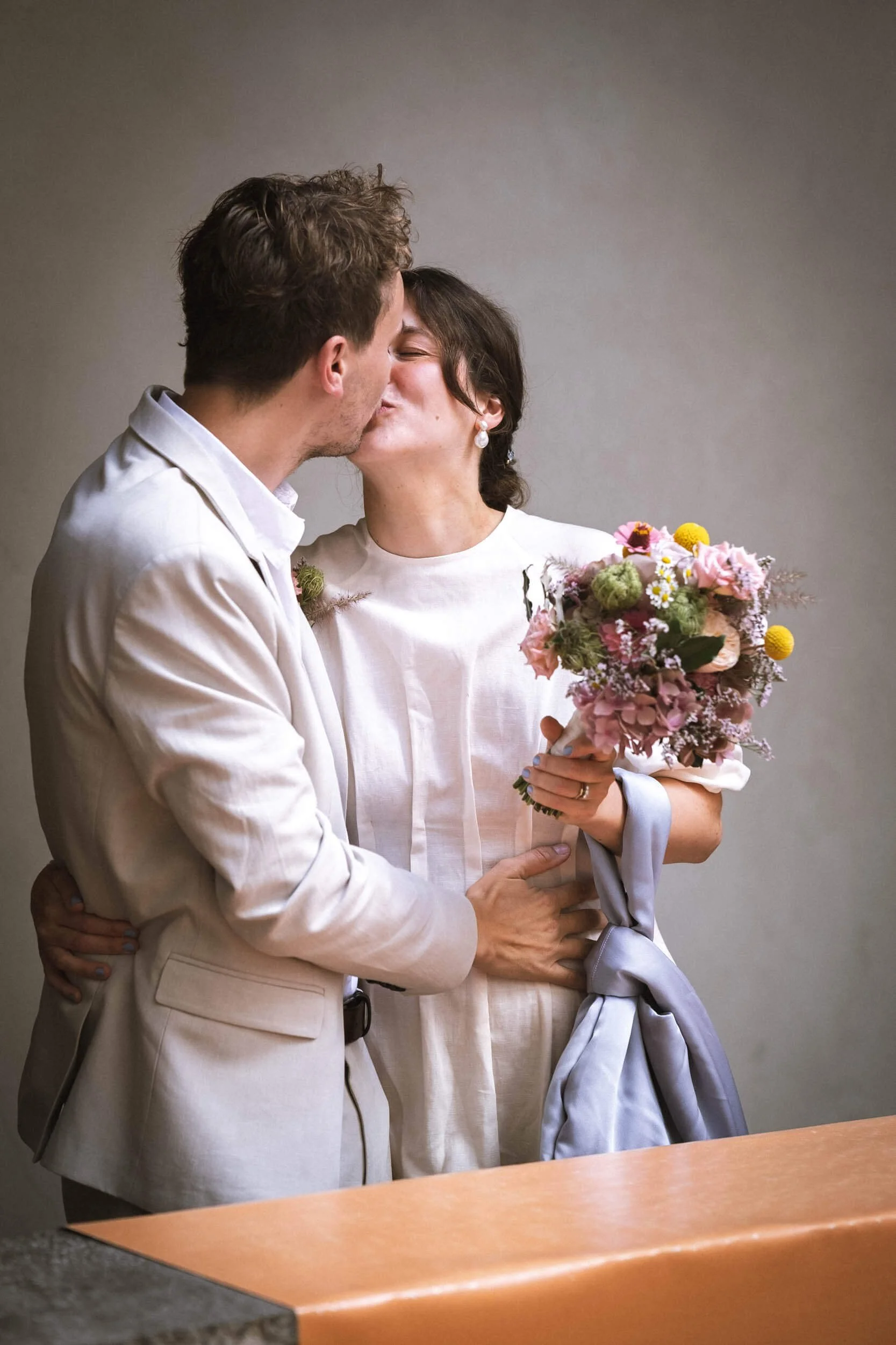 Ein Paar küsst sich bei einer Hochzeit, die Frau hält einen Blumenstrauß in der Hand.
