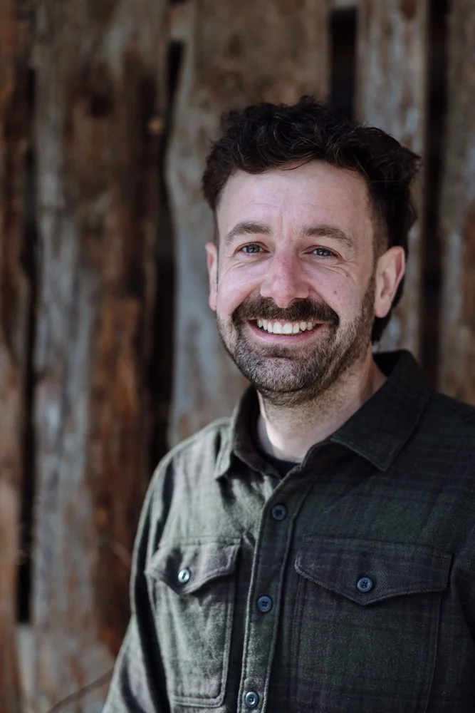 Lächelnder Mann vor Baumstämmen im Freien