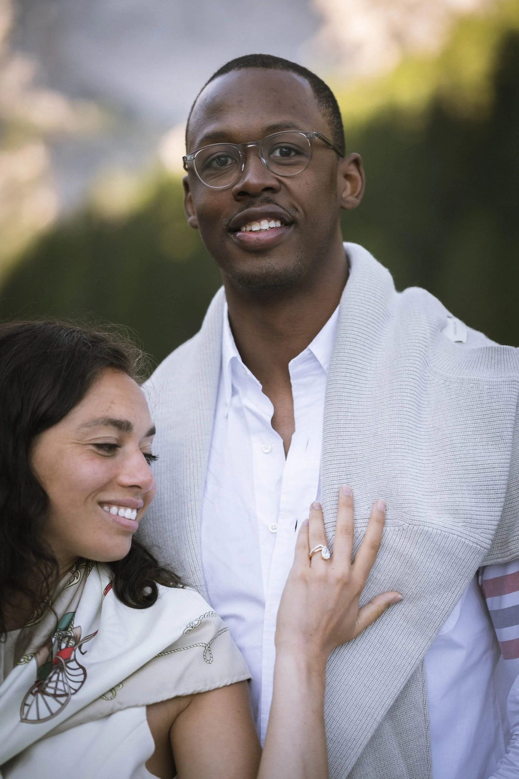 Ein lachendes Paar im Freien, der Mann trägt eine weiße Hemdjacke, die Frau hat einen Ehering und eine weiße Bluse mit buntem Muster.