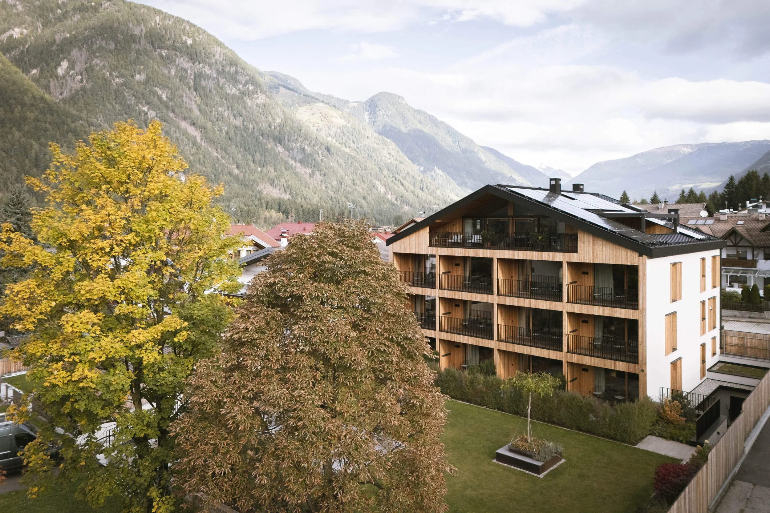 Mehrstöckiges modernes Wohngebäude mit Holzverkleidung, umgeben von Bäumen und eingefasst von Bergen in der Ferne.