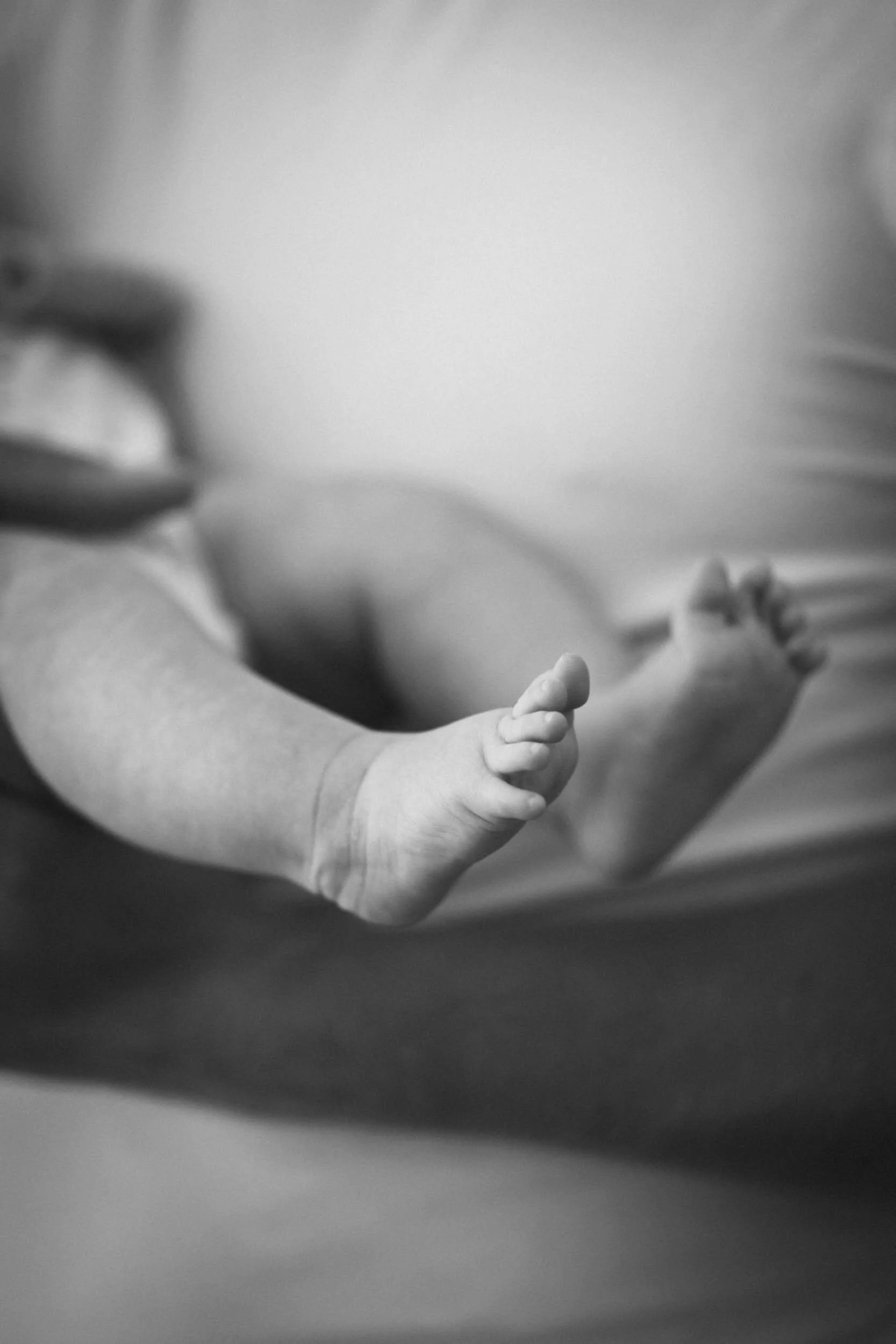 Schwarze und weiße Nahaufnahme eines Babyfußes, das auf einer weichen Oberfläche liegt.