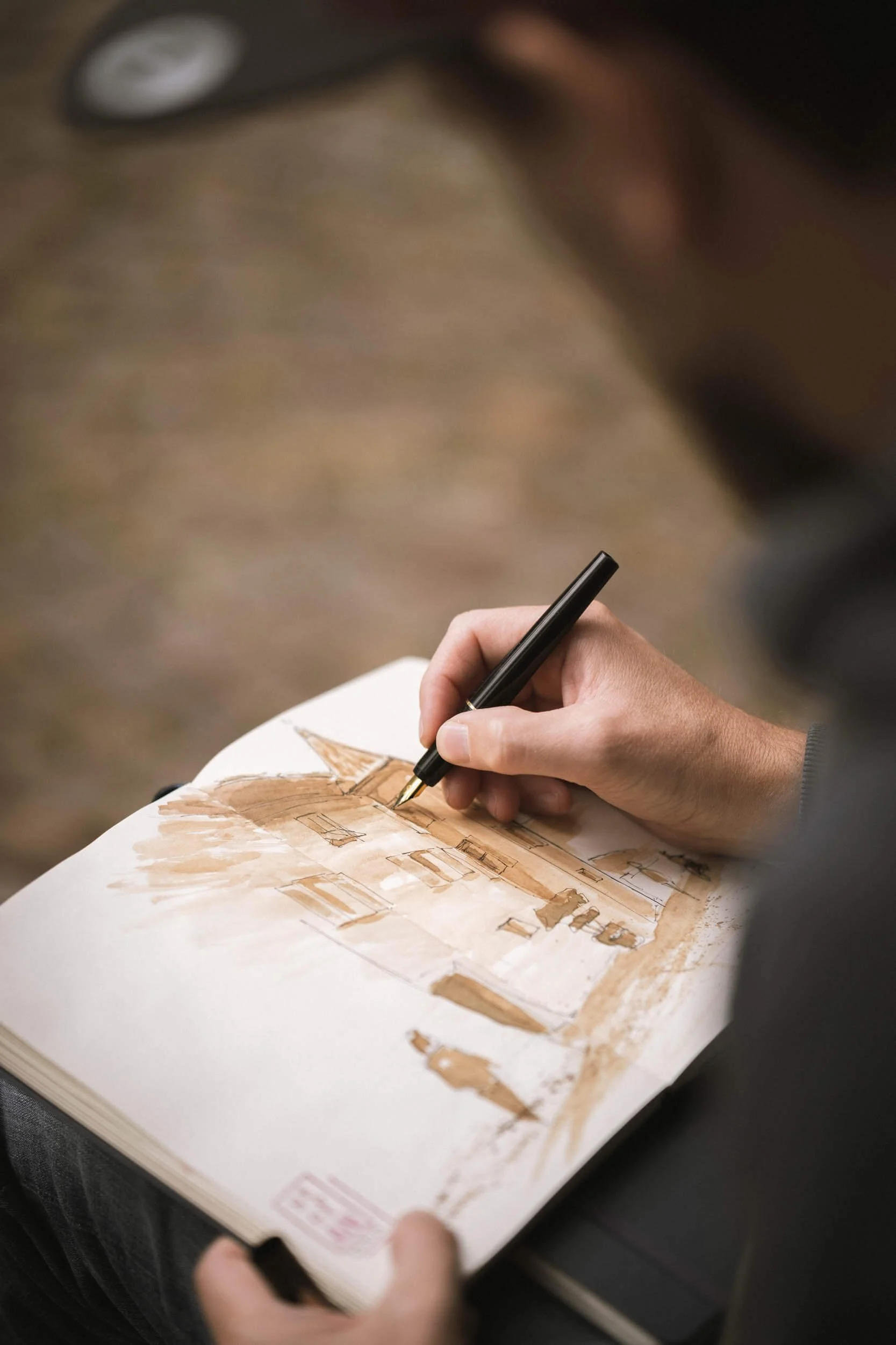 Person malt eine Architekturzeichnung eines Gebäudes mit Aquarellfarben in einem Skizzenbuch.