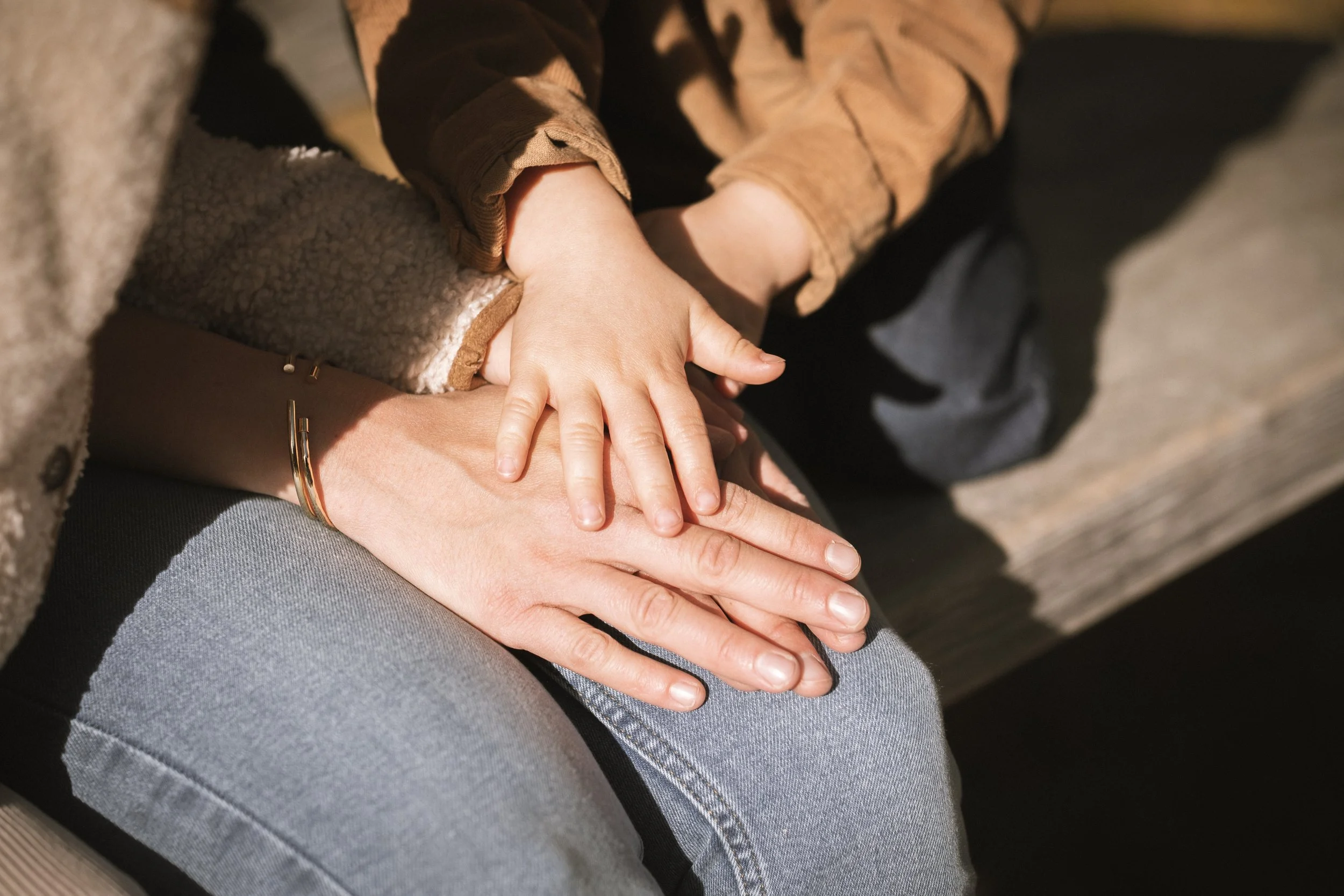 Nahaufnahme von einer erwachsenen Hand, die eine Kinderhand hält, während beide auf einem Sitz sitzen.