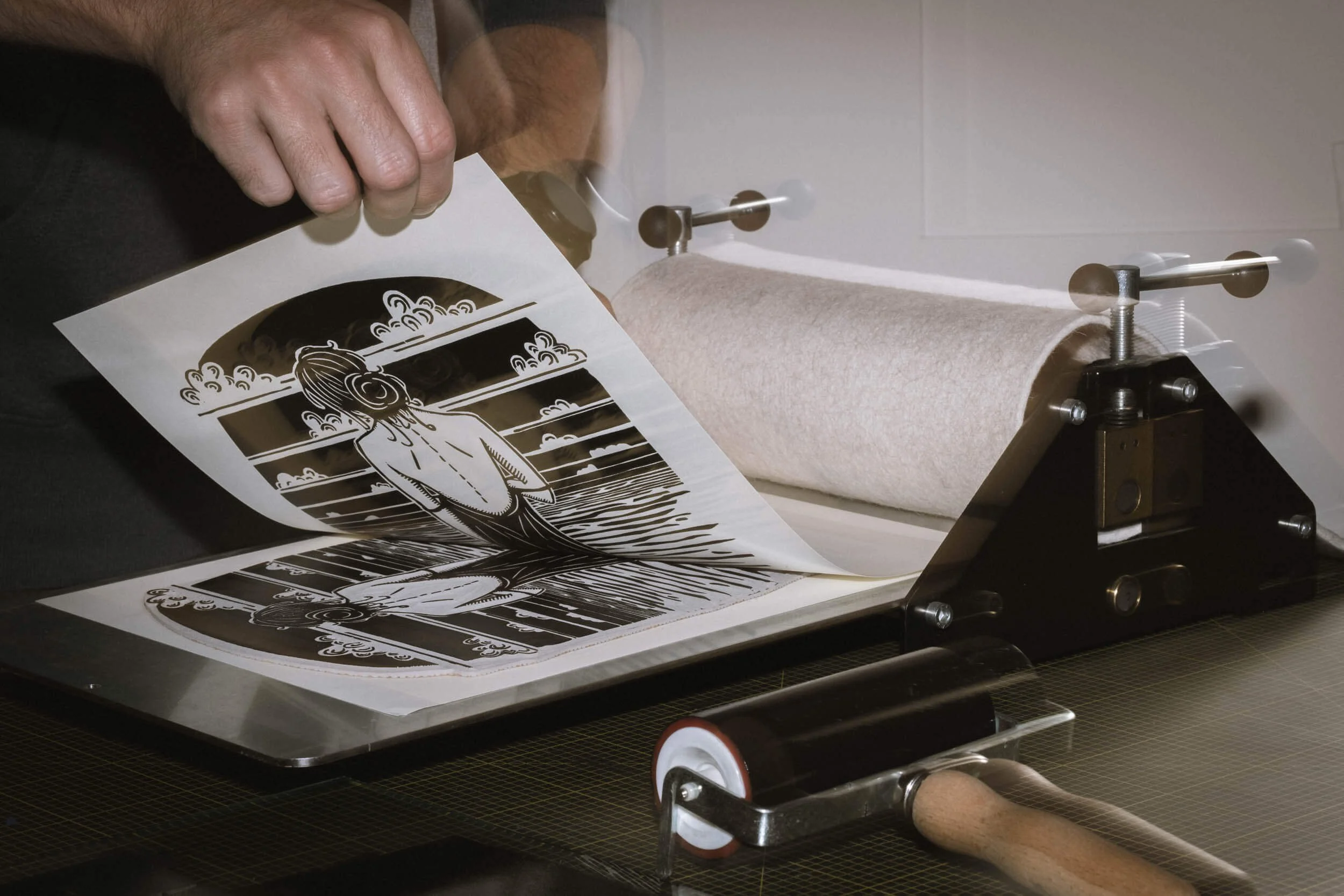 Ein Siebdruckautomat mit einer Druckplatte, auf der schwarze und weiße Drucke eines männlichen Charakters vor einem Himmel mit Wolken und Wasser zu sehen sind.
