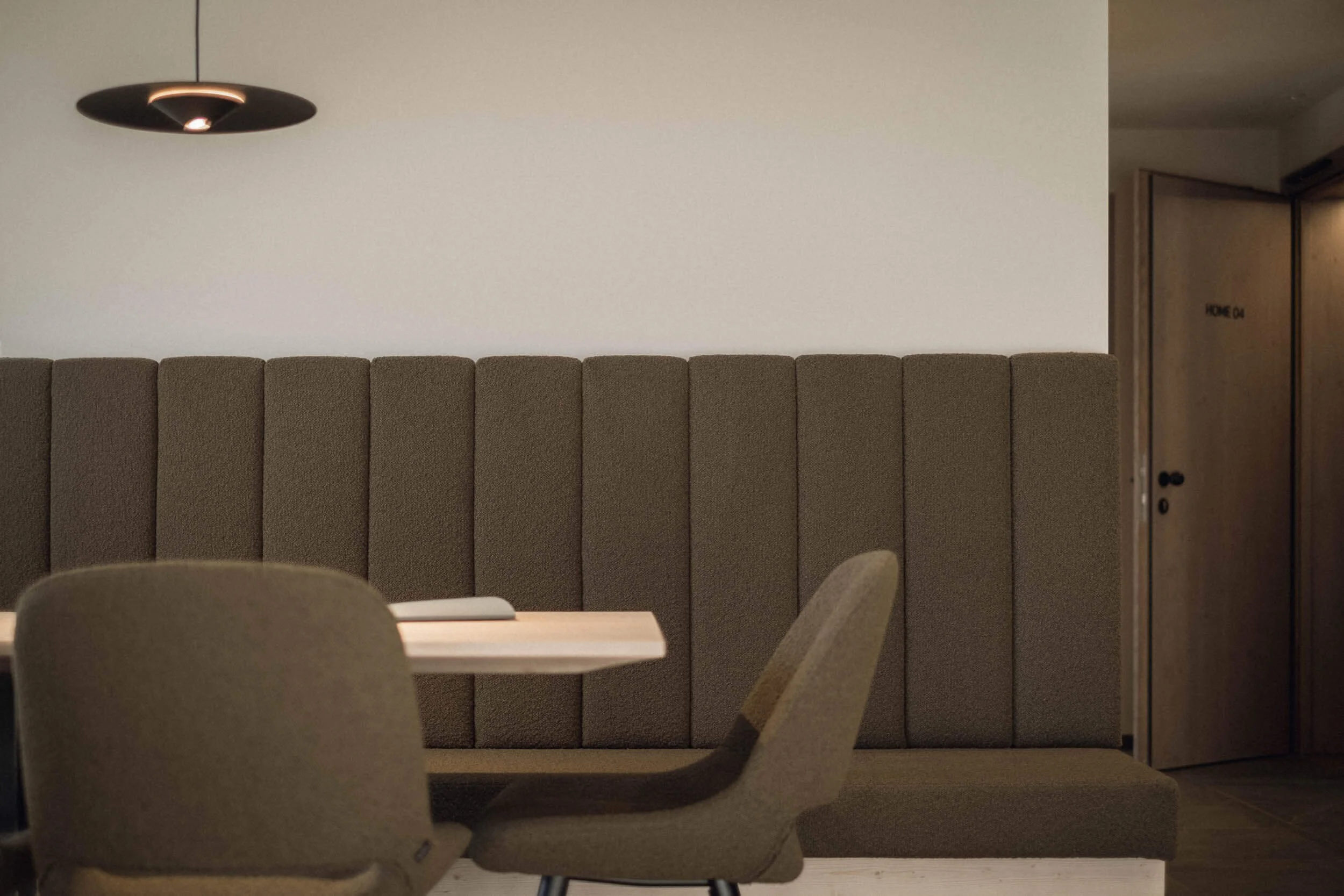 Innenraum mit beige-braunen Stühlen und einer hohen, gepolsterten Trennwand; an der Tür steht 'HOME 04'.