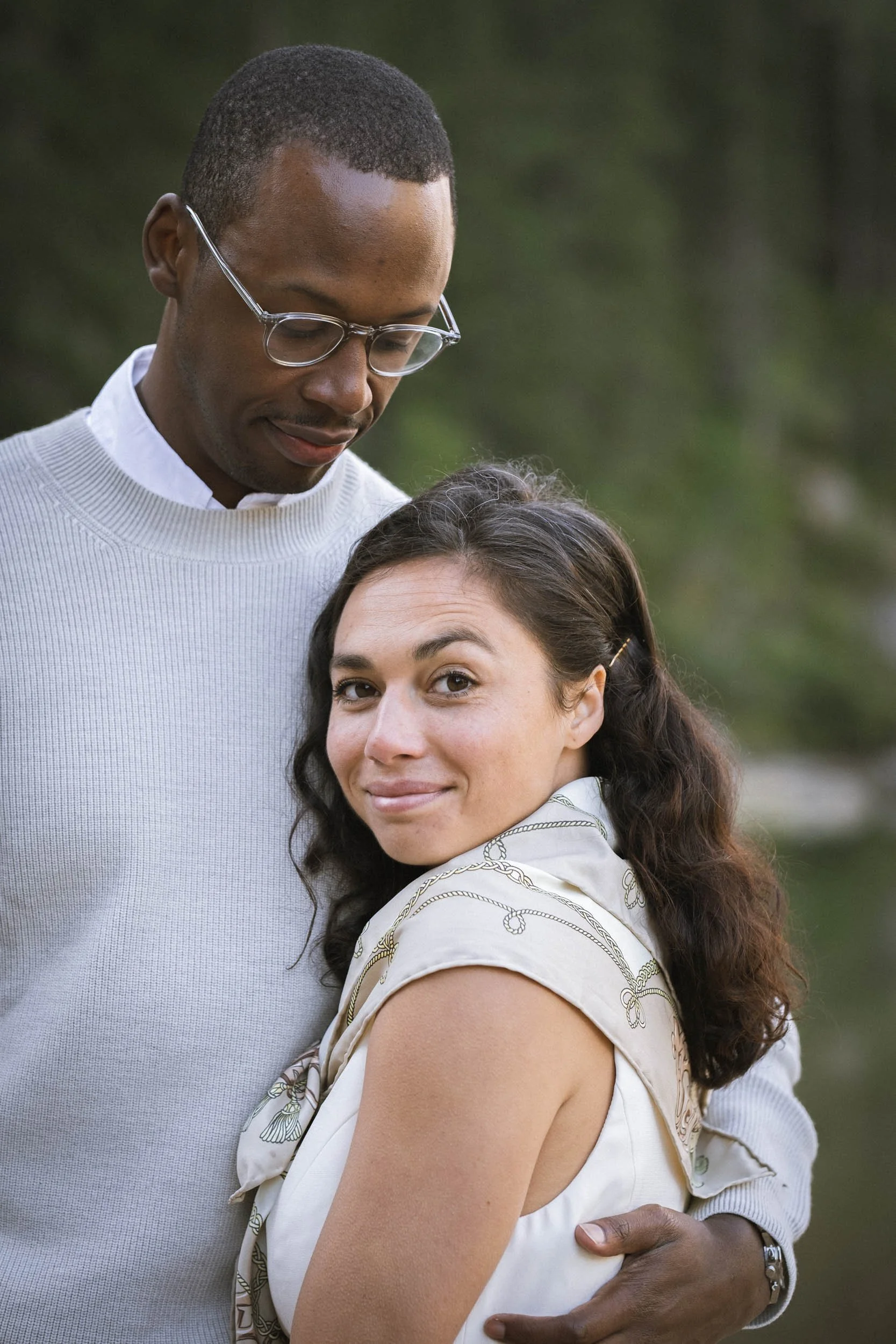 Ein Mann mit Brille umarmt eine lächelnde Frau im Freien.