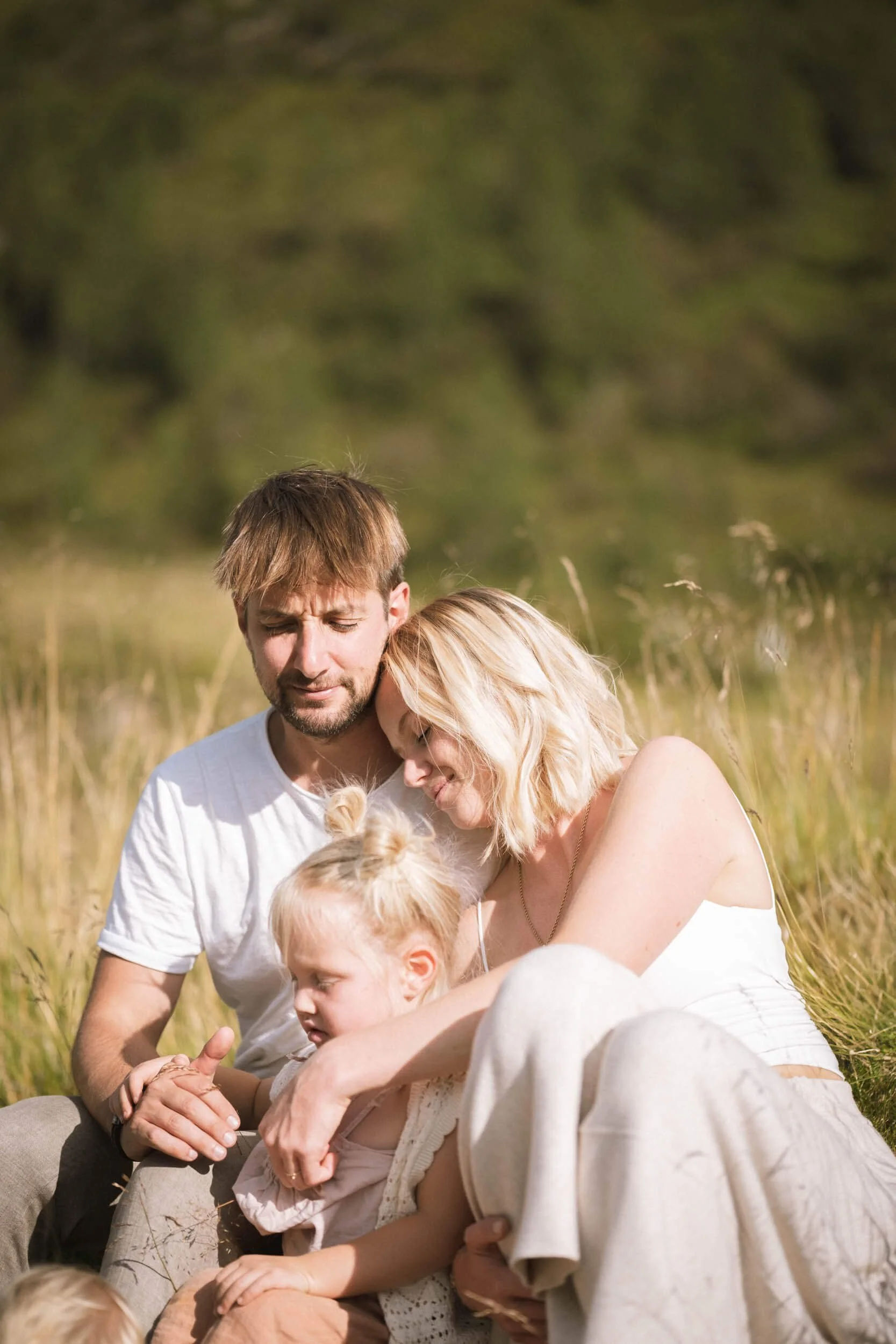 Familie im Grünen, sitzend in der Sonne, nah beieinander, liebevoll.