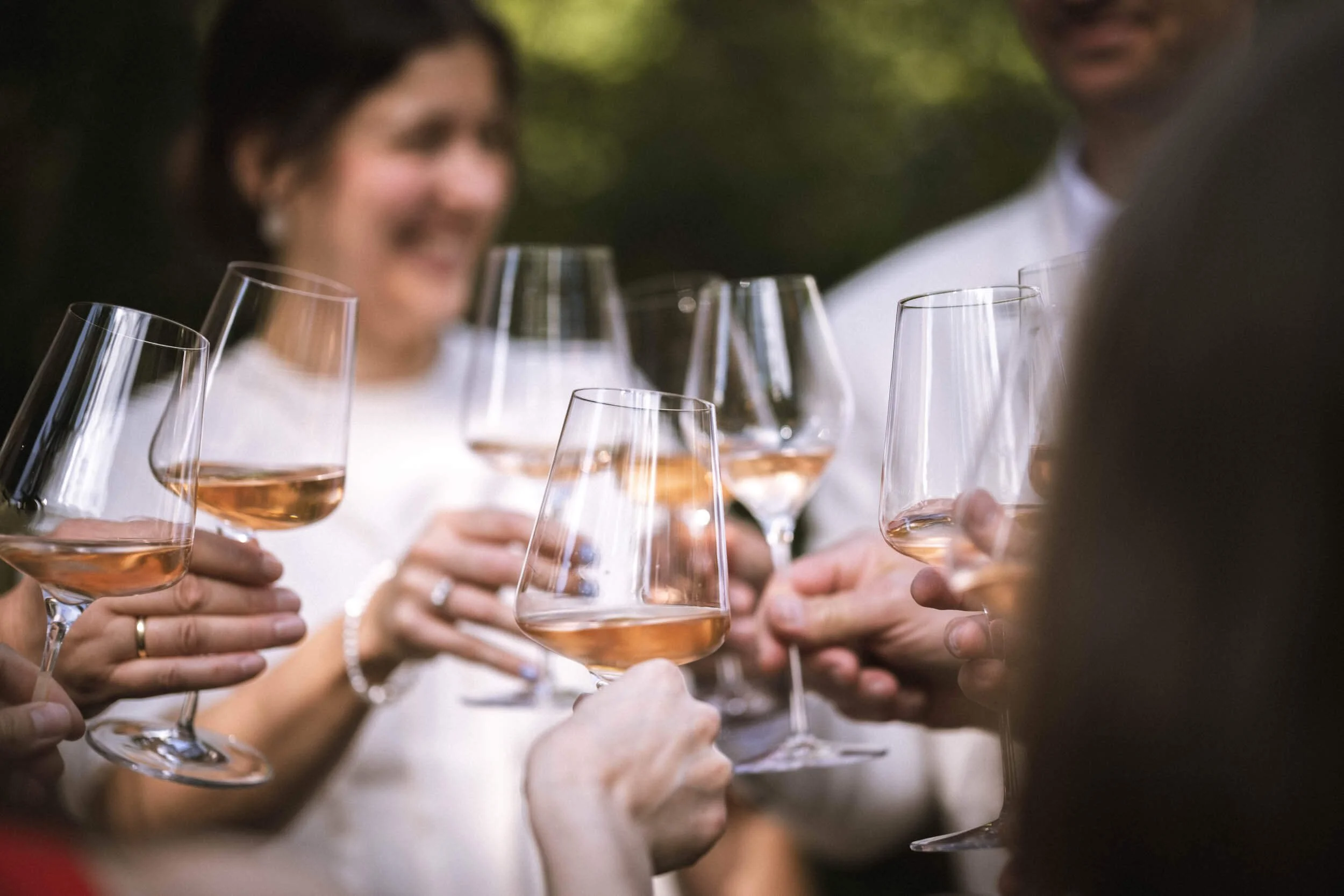 Menschen bei einem Fest trinken Rosewein aus Weingläsern, im Freien mit Bäumen im Hintergrund.