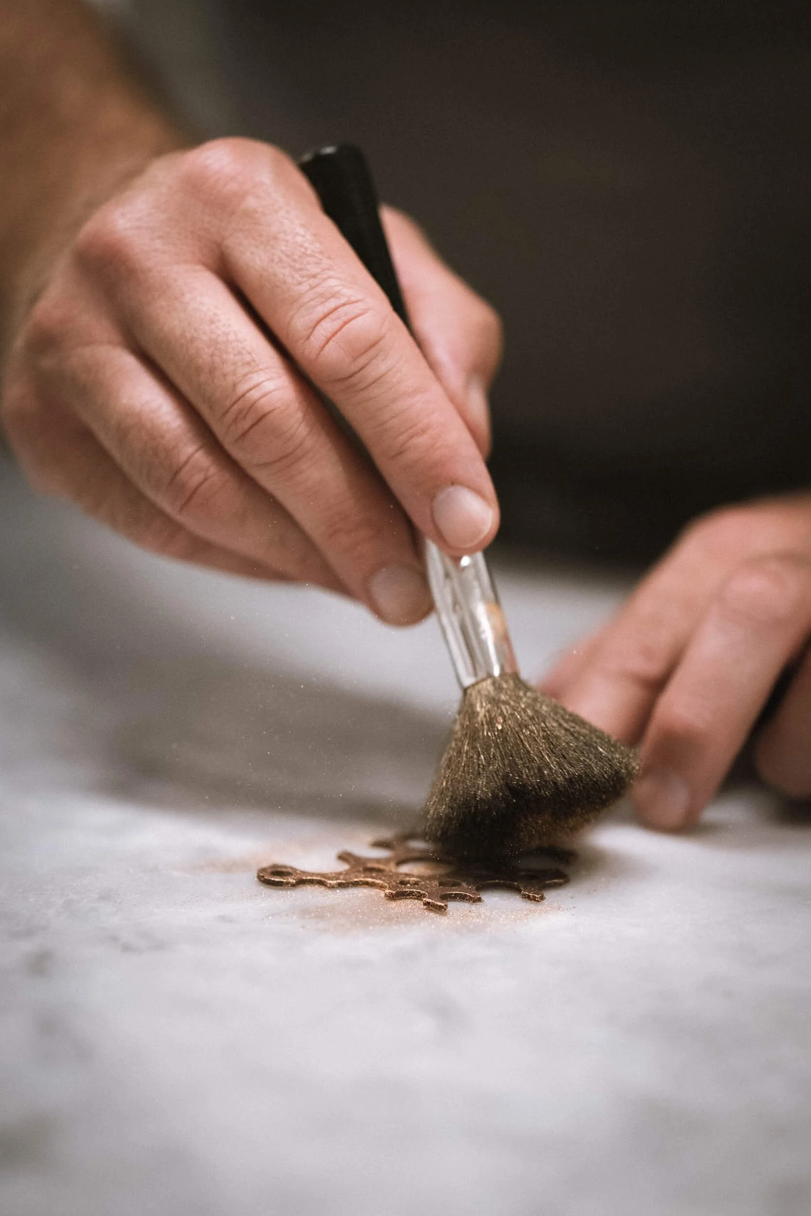 Hand arbeitet mit Werkzeug auf einer Oberfläche, vermutlich bei der Herstellung von Metallteilen.