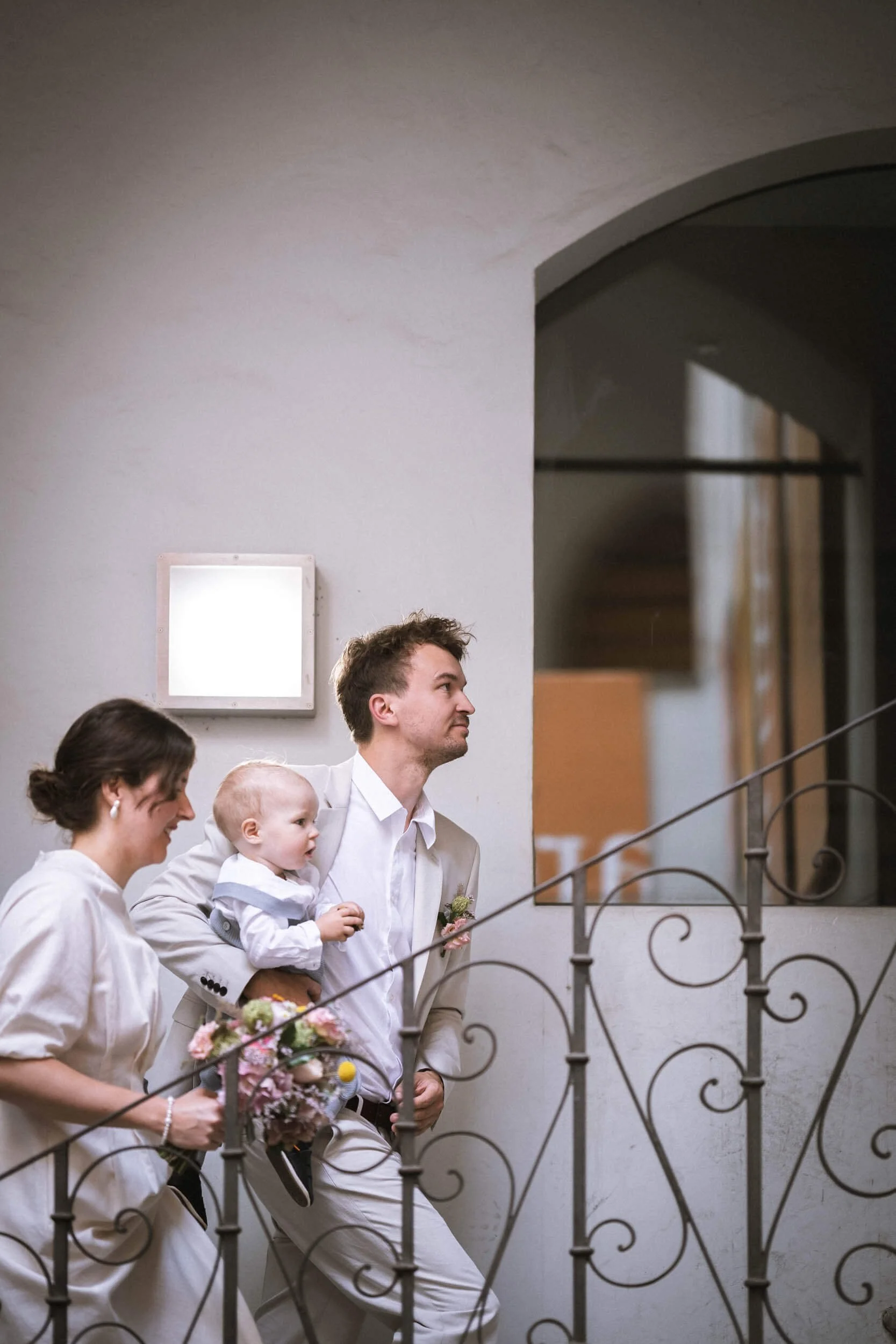 Ein Mann, eine Frau und ein kleiner Junge beim Aufstieg auf eine Treppe in einem hellen Raum.