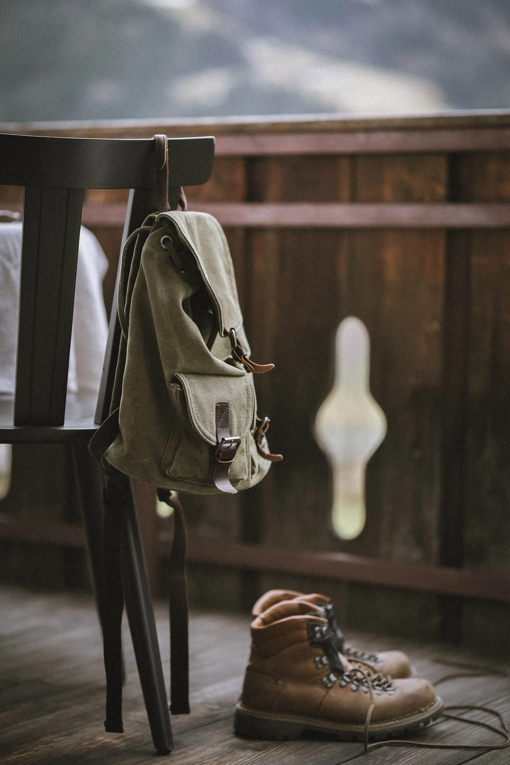 Ein grüne Rucksack hängt an einem Stuhl, braune Lederstiefel liegen auf dem Holzboden.